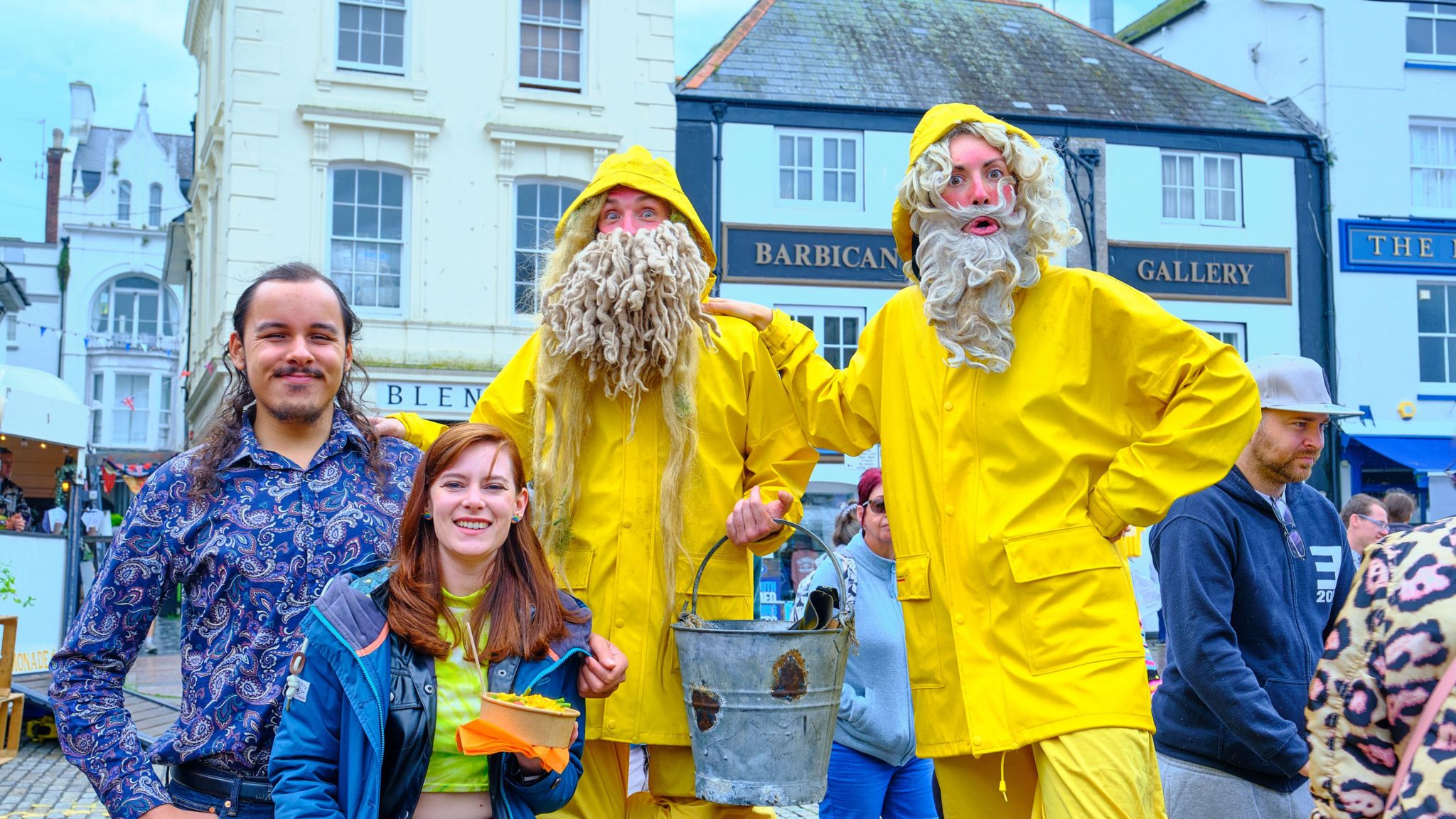 A photo which shows two people stood next to two other people wearing yellow fisherman outfits with fake white beards. One is holding a bucket.