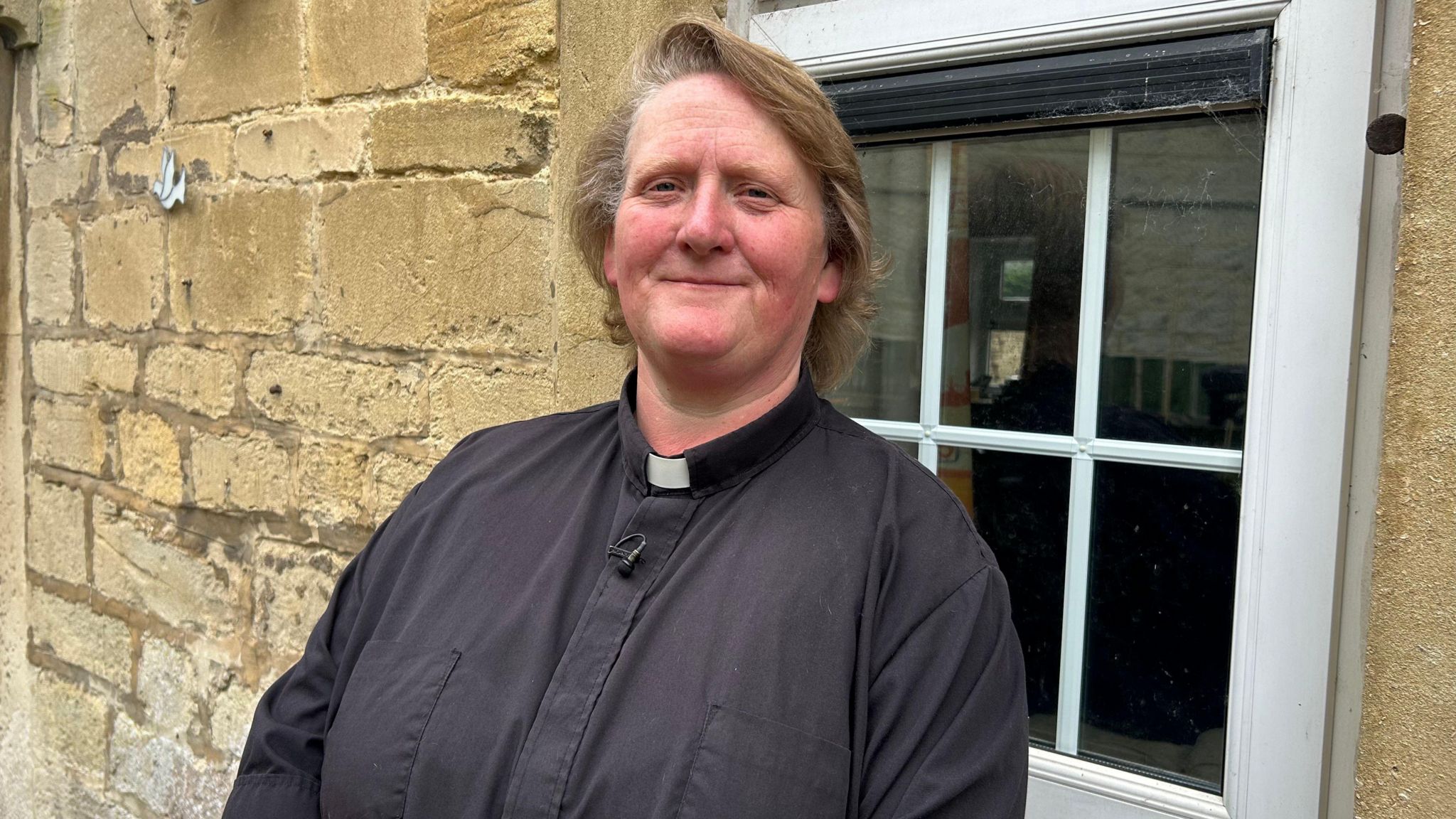 Clair Southgate stood in front of a window wearing her black cassock