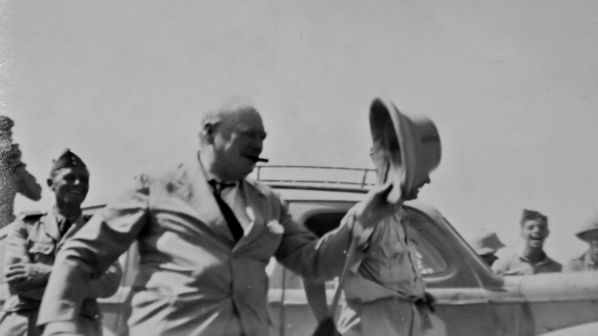 An old photograph of Sir Winston Churchill with a cigar in his mouth waving his hat as he visits troops