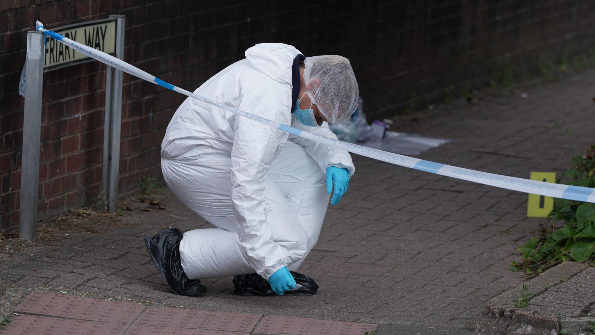 Someone in a white hazmat suit bending down towards the pavement.