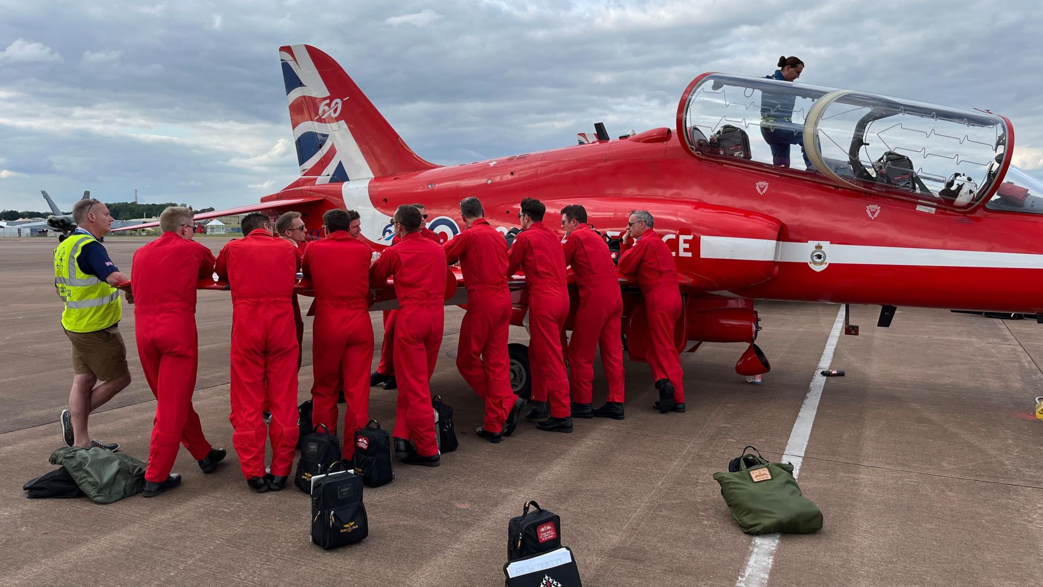 Red Arrows pilots and crew gather around the wing of one of their aircraft 