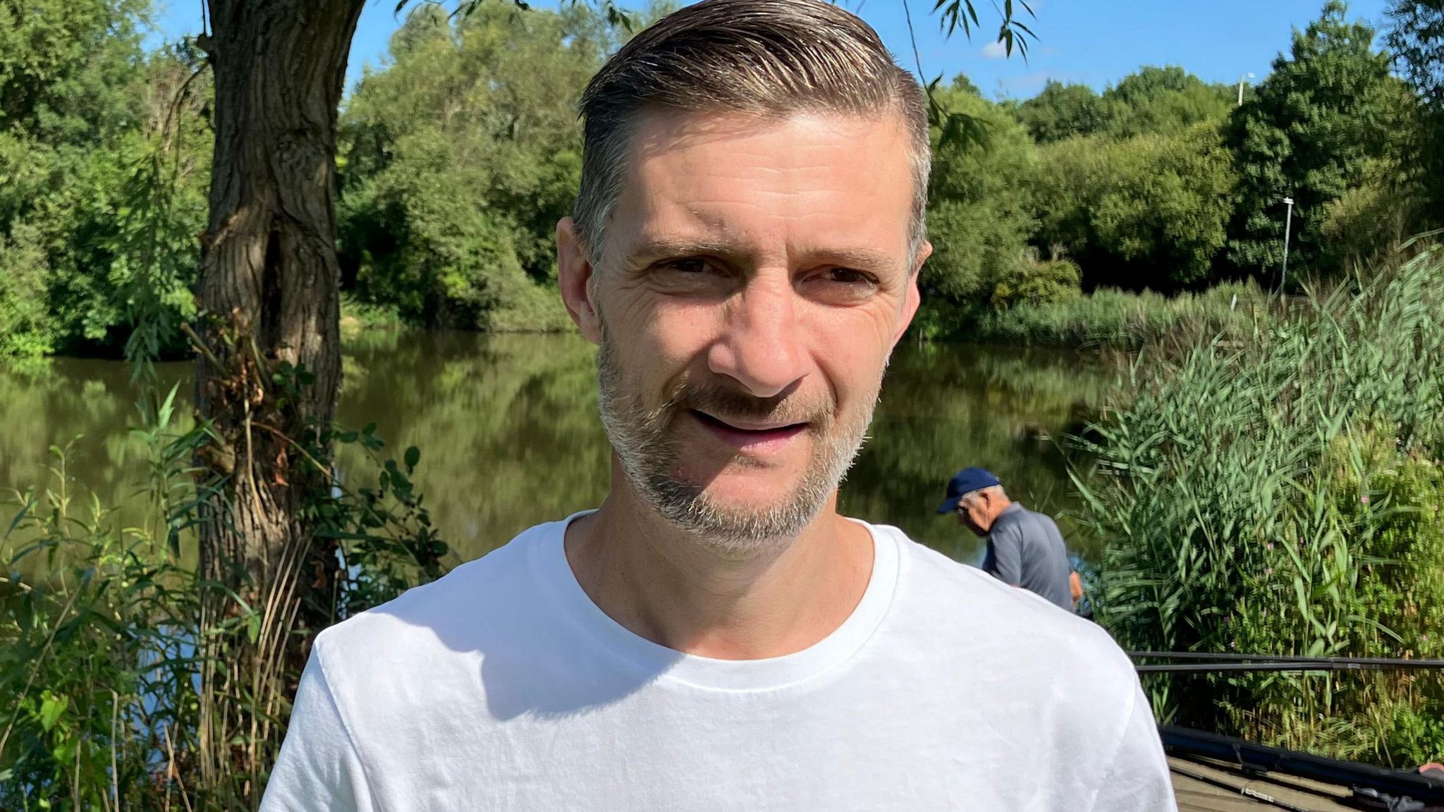 Lee Fitzgibbon in front of the lake on a sunny day wearing a white t-shirt