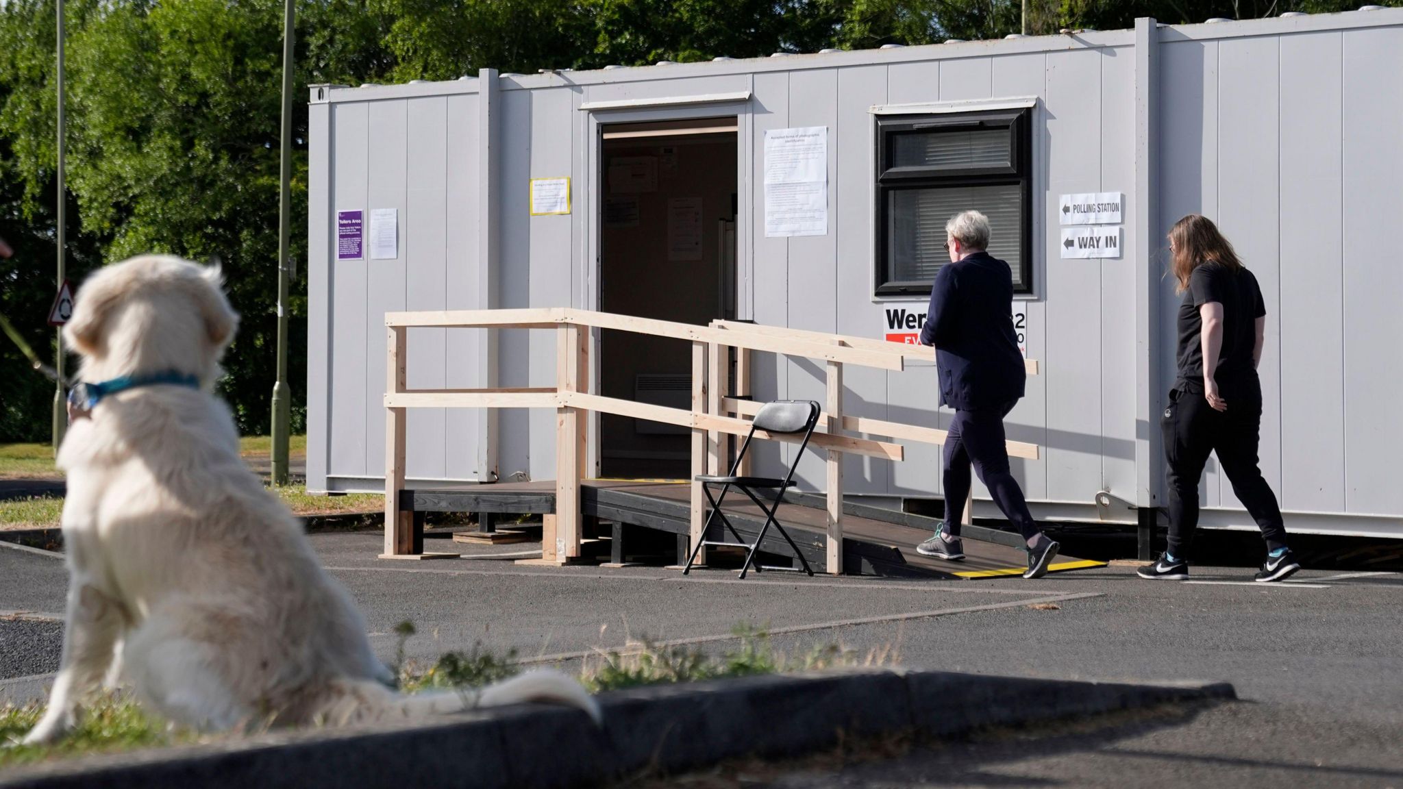 People arrive to cast their vote at a polling station in a temporary building in Andover, Hampshire. The back of a white dog can be seen as it is staring at the people walking into the polling station