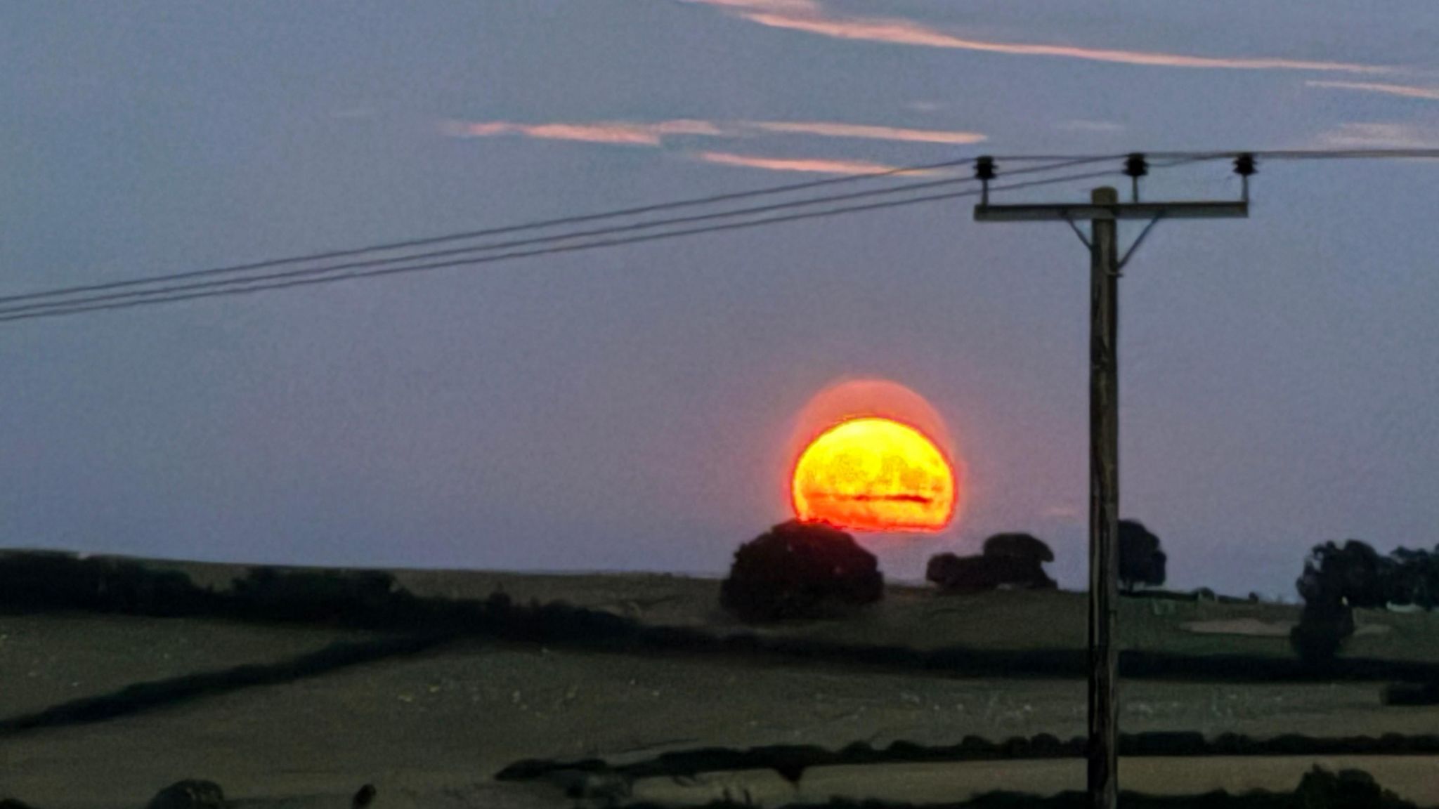 A long exposure image showing a glowing orange moon against a dark landscape of fields and trees