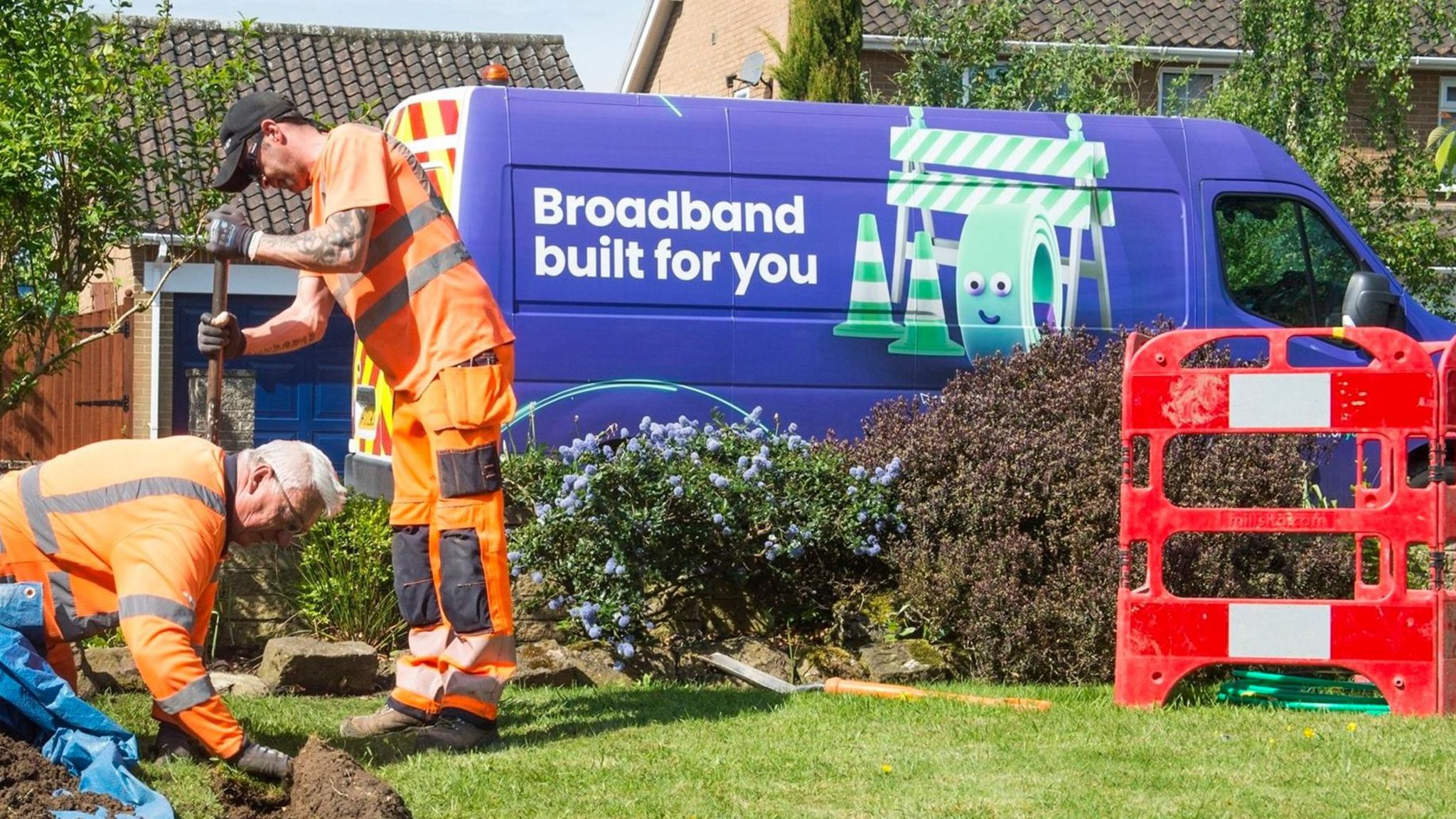 Two contractors in orange high-vis vest digging a lawned garden. In the background there is a red barrier and purple van with the words: 'Broadband built for you' on it