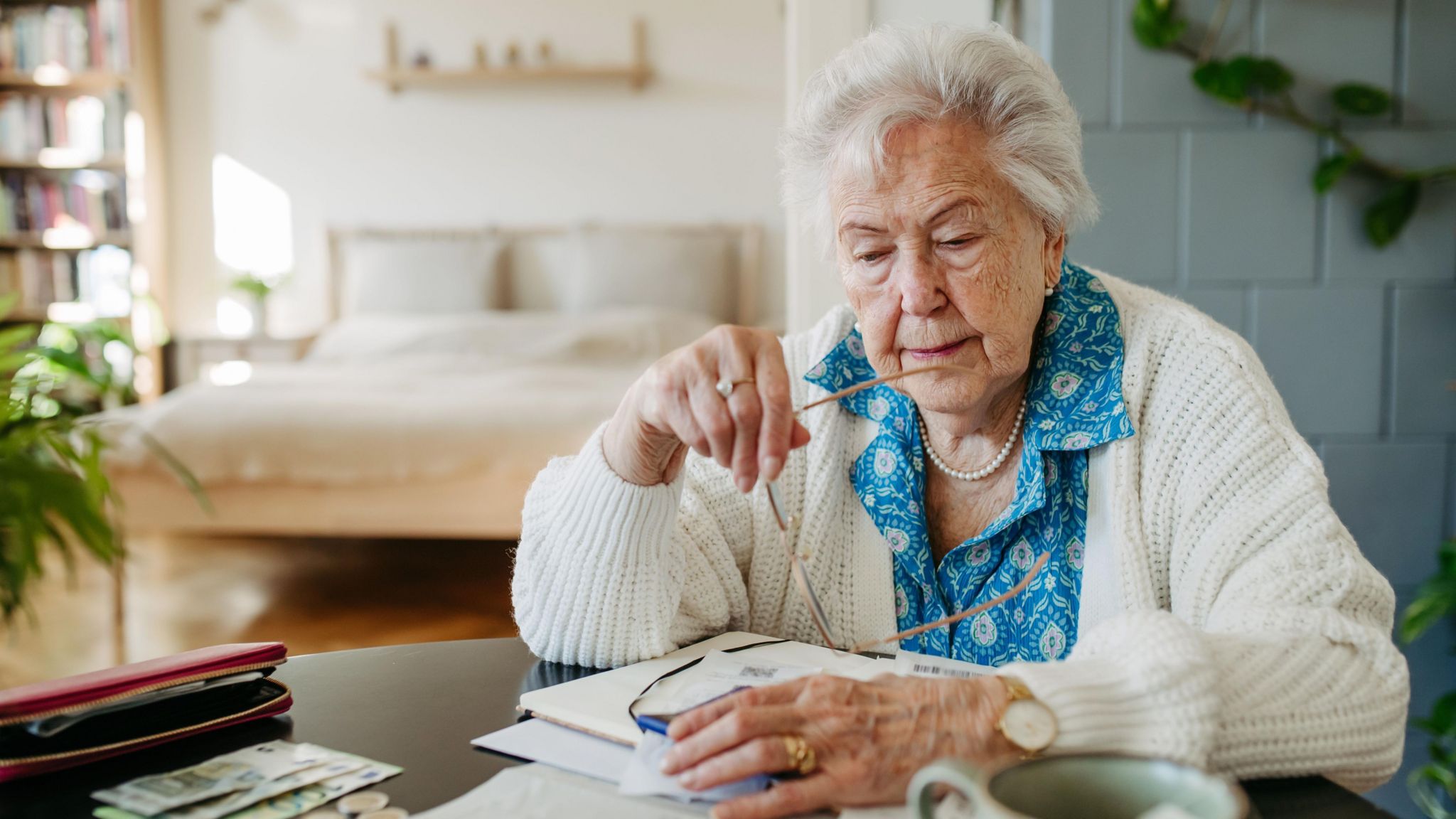 Image of an elderly woman sat at a table with paperwork and bank notes.