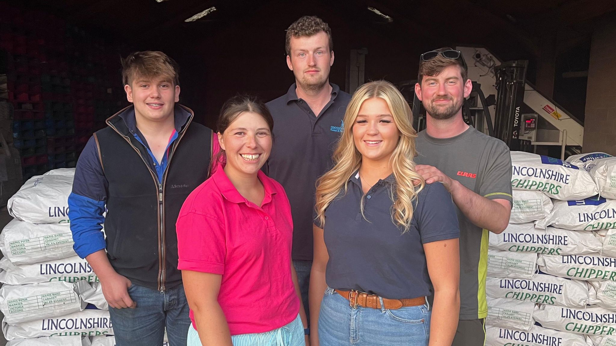 Five members of Corringham Young Farmers' Club three men at the back and two women at the front with bags of Lincolnshire Chippers in the background