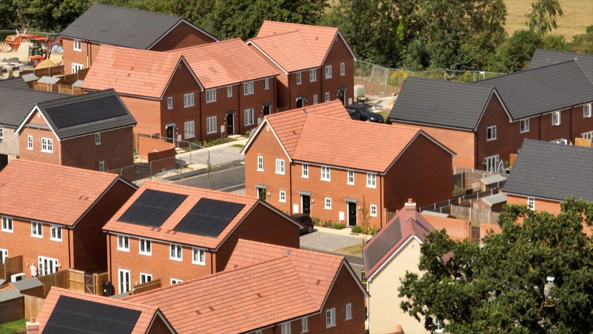 An aerial picture of newly-built homes in Bacton. They are all made from red brick and have red or grey tiled roofs. Their white window frames are clearly seen in the sunshine. Three of the houses have solar panels visible and there are signs of construction work still going on.