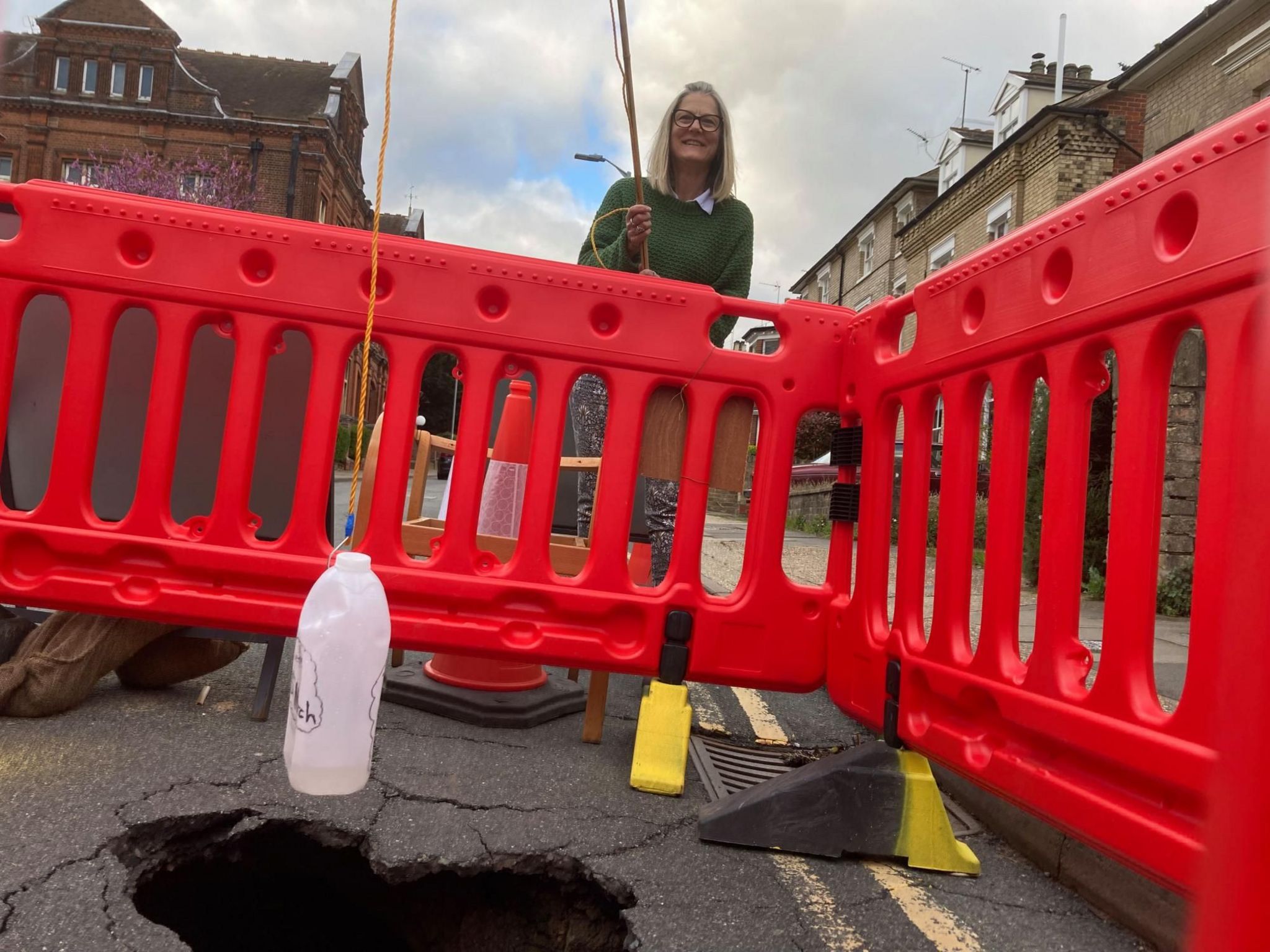 Lindsey Ward holding a mocked-up fishing road over a sinkhole on Ipswich's High Street