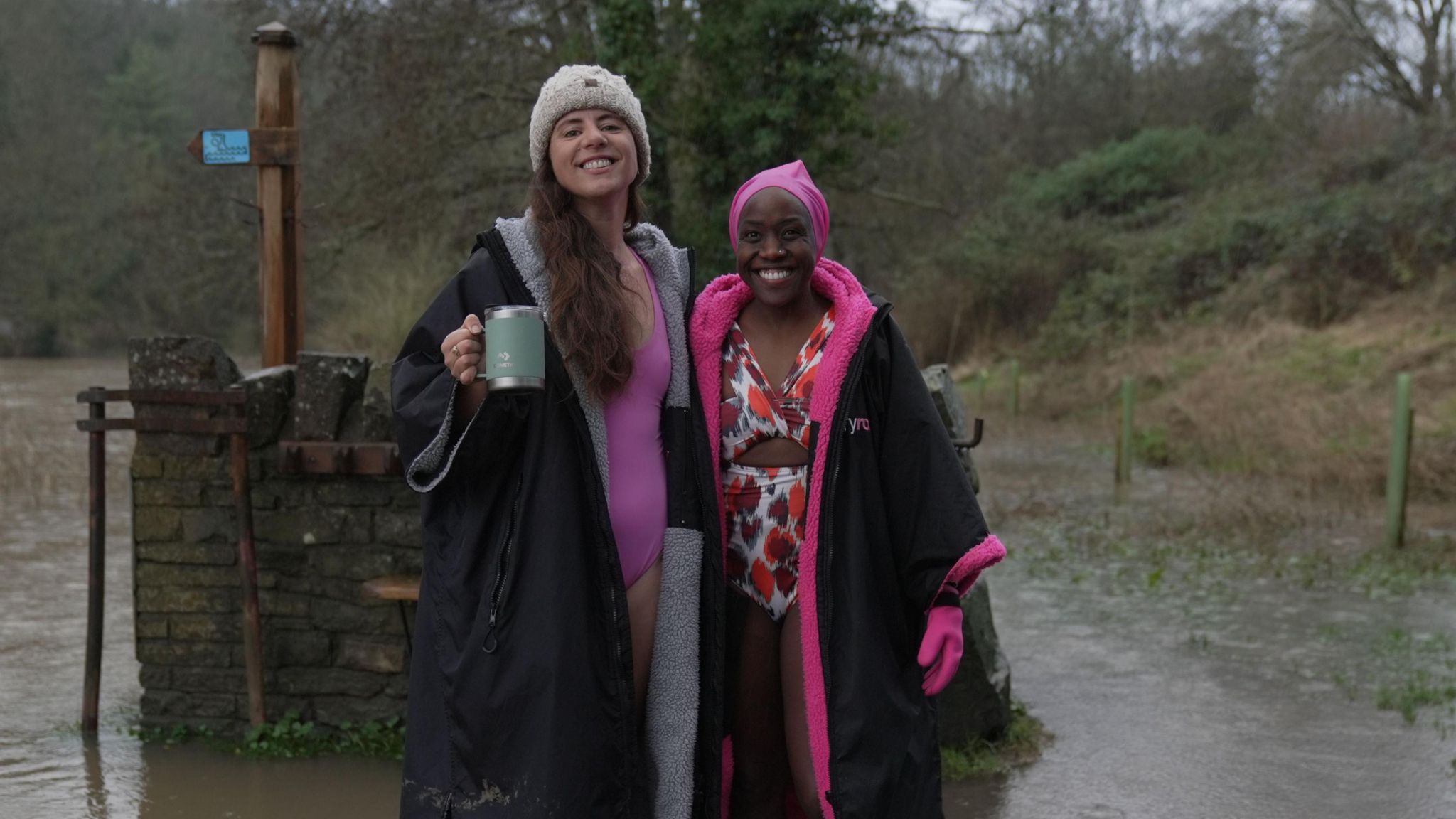 Charlotte Sawyer and Aggie Nyagari standing by the Avon. They are wearing swimsuits with smim robes over the top. They are smiling and looking into the camera