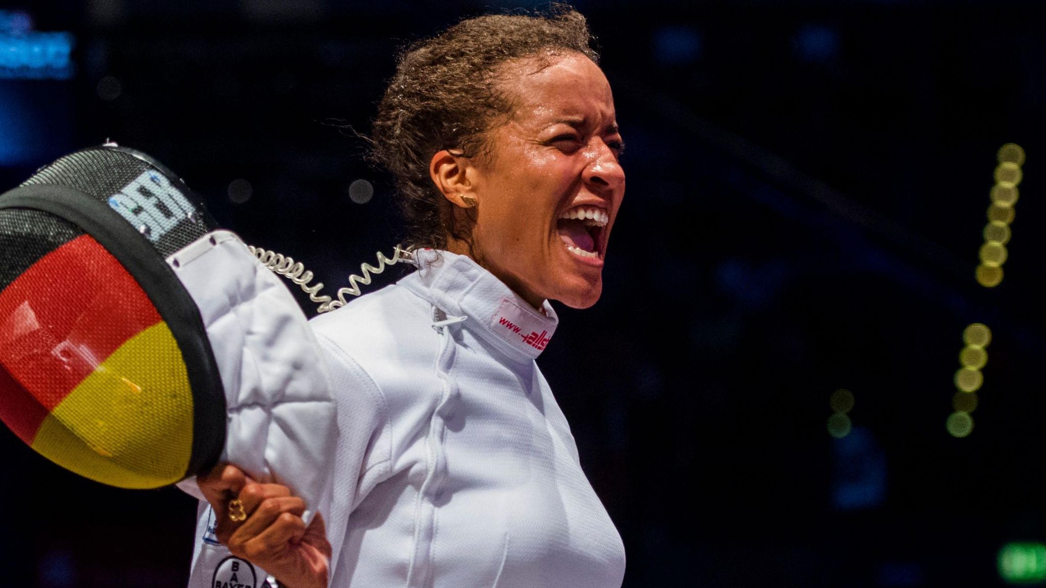 Alexandra Ndolo closes her eyes and screams after winning a fencing match, holding her helmet with visor in colours of the flag of Germany