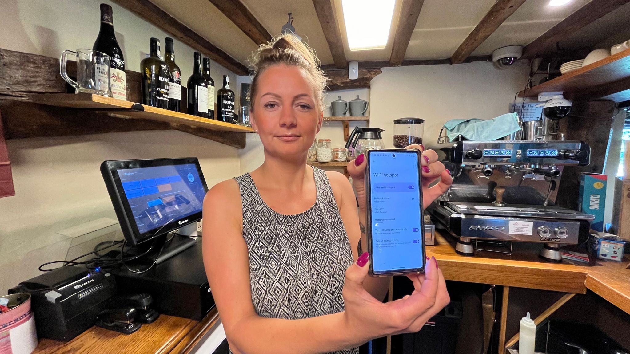 Tess Wright holds up her mobile phone at the camera, while standing beside one of the cash registers at the pub. 