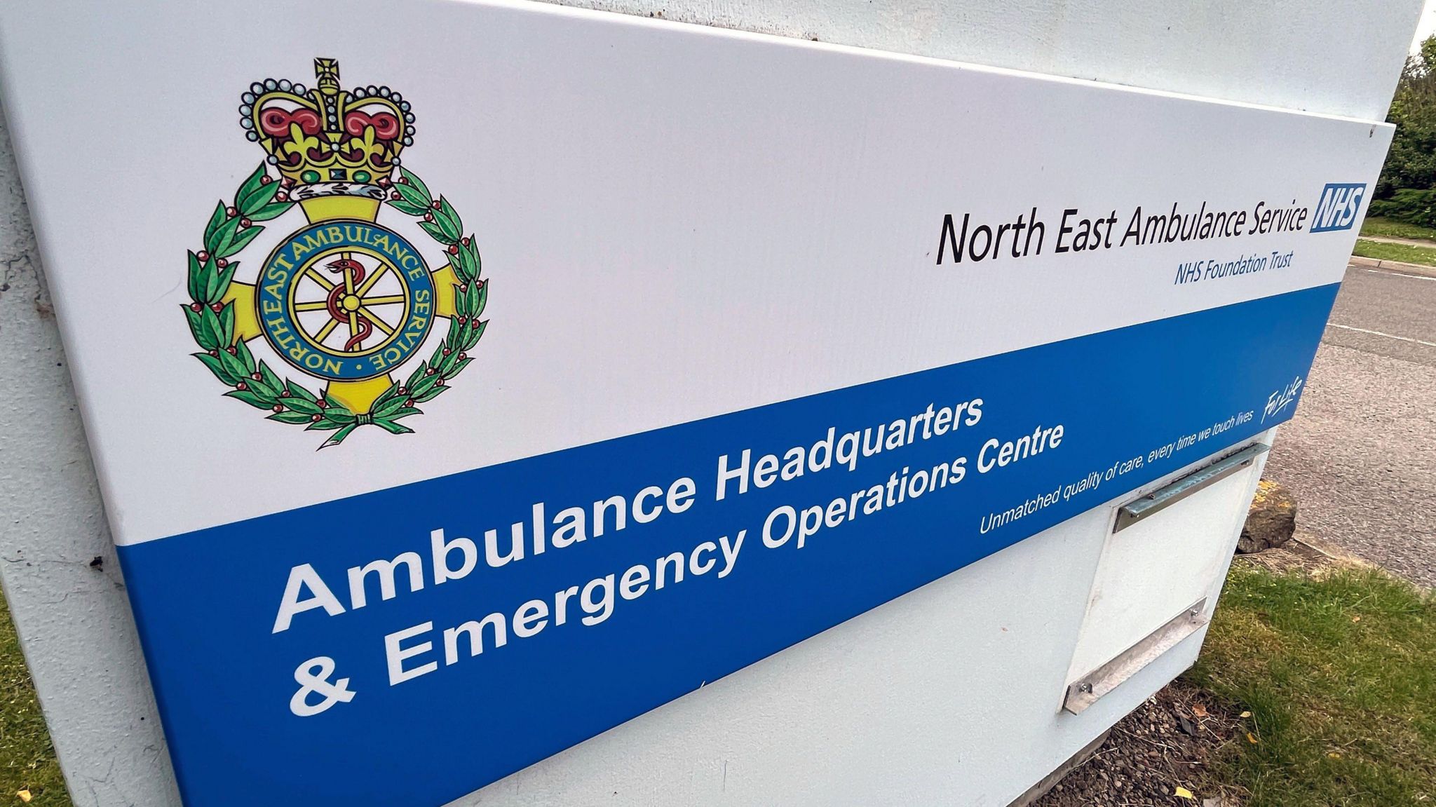 A blue and white sign saying "North East Ambulance Service, Ambulance Headquarters & Emergency Operations Centre" and with the ambulance badge on it.