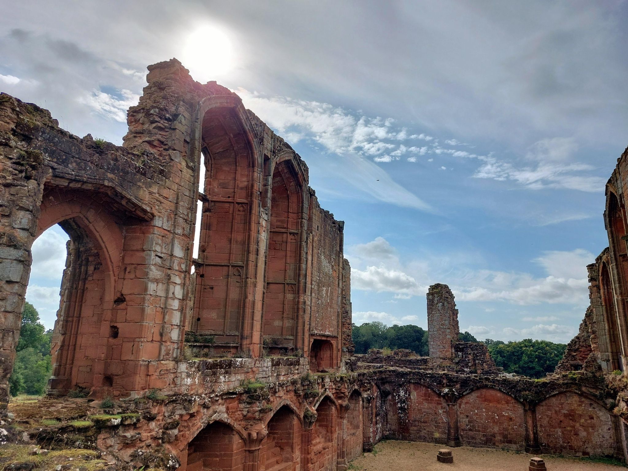 Ruins of Kenilworth Castle under a blue sky with light white clouds and hazy sunshine.