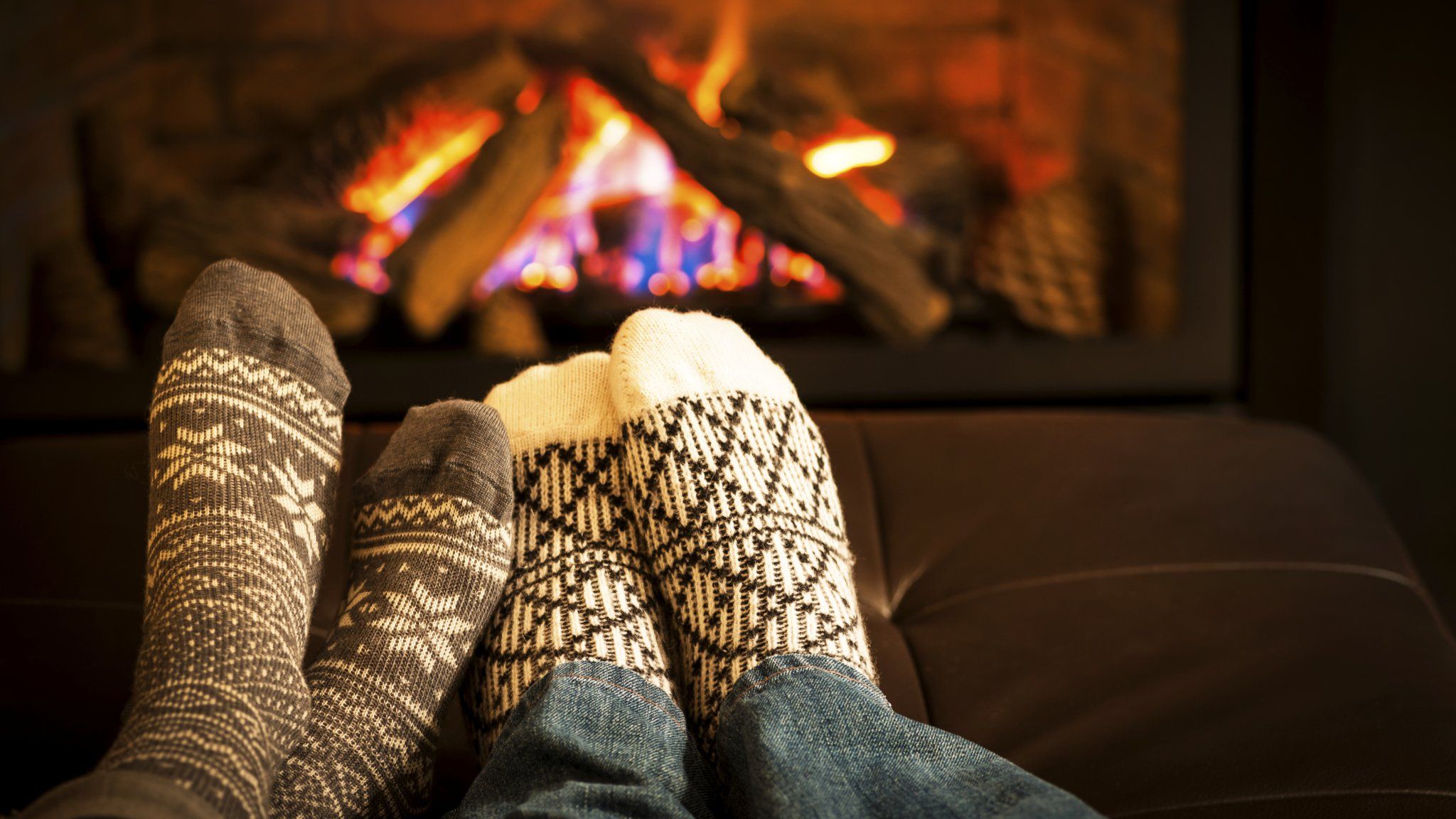 Two pairs of feet in socks in front of a roaring fire