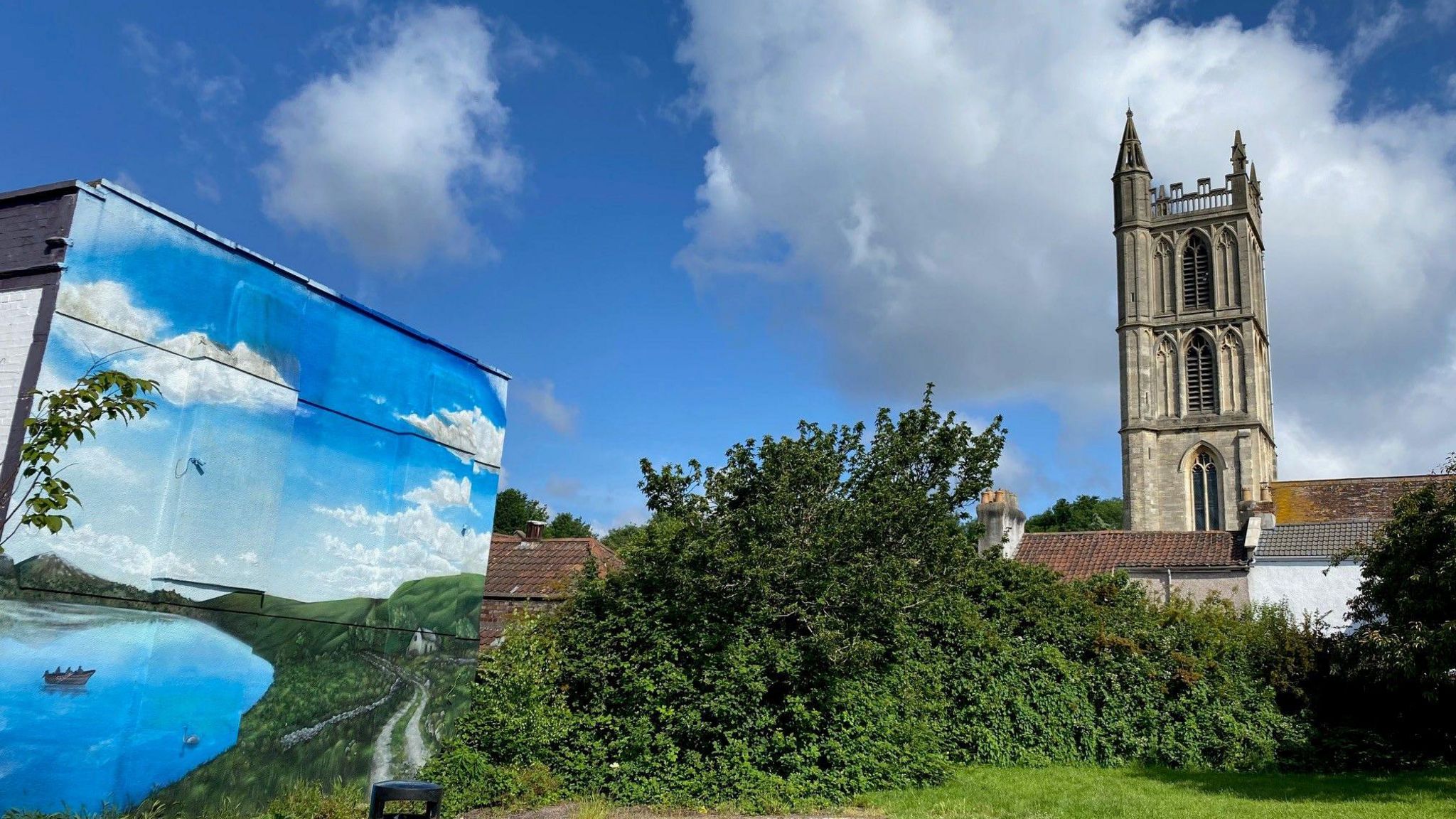 A mural depicting a blue lake and blue skies, next to a church in St Werburghs, Bristol