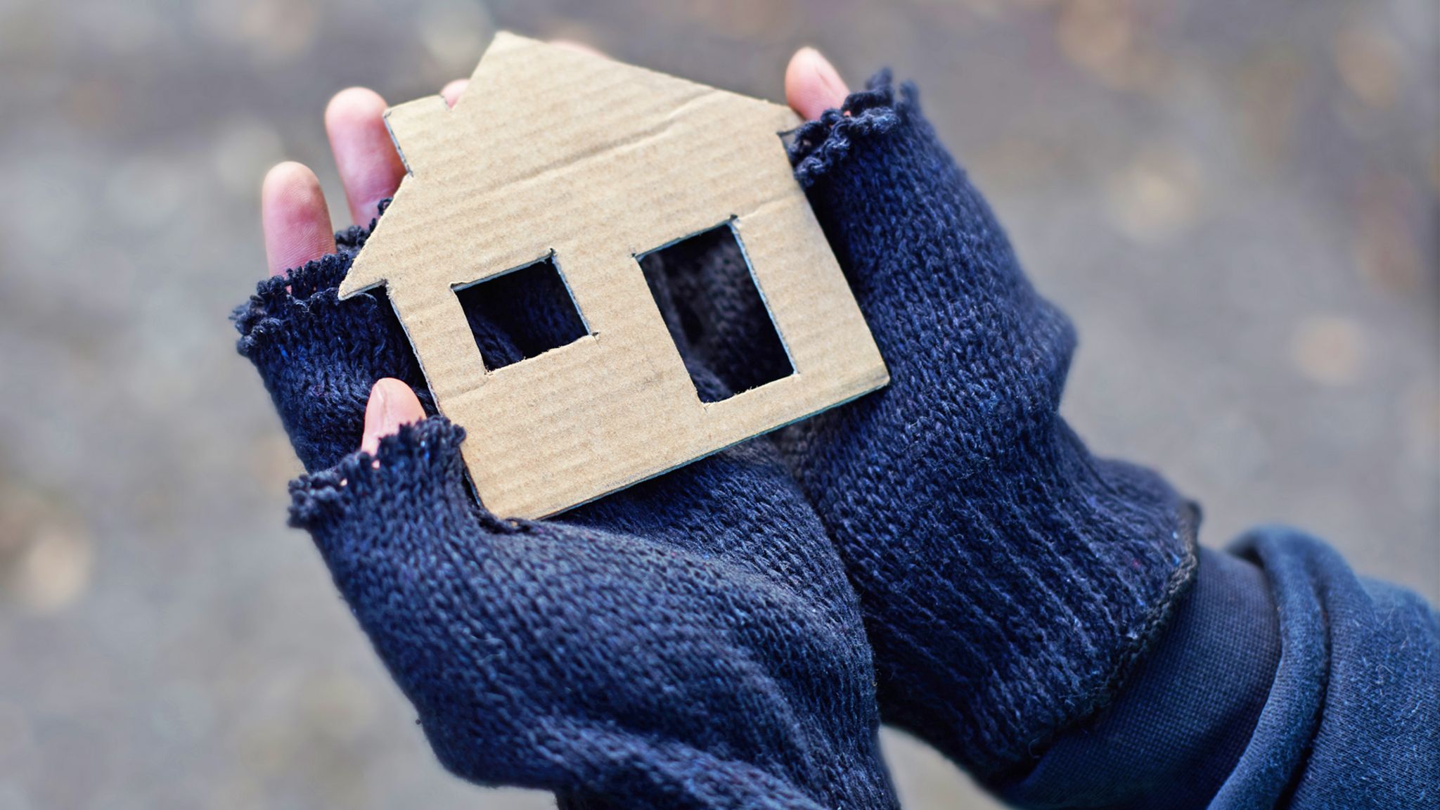 Gloved hands holding a cardboard cut out of a house