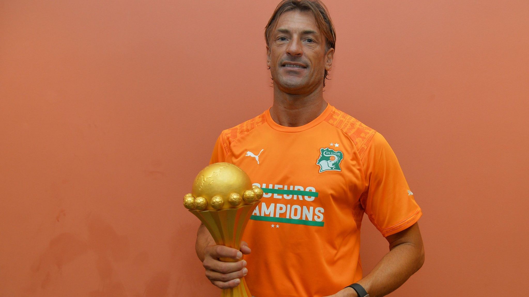 Herve Renard, wearing a bright orange Ivory Coast T-shirt, holds the Africa Cup of Nations trophy