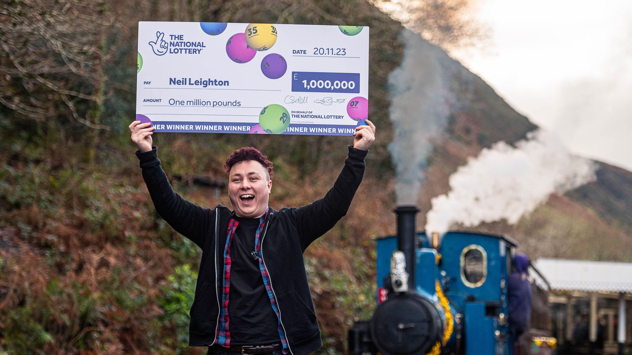 Neil Leighton holds a large cheque above his head