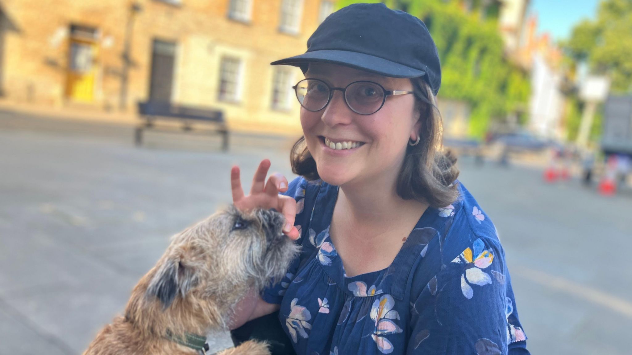 Isabelle Phillips, wearing a blue cap, has shoulder length brown hair and a blue top with a flower print. Her dog Peggy is seemingly being fed a dog biscuit