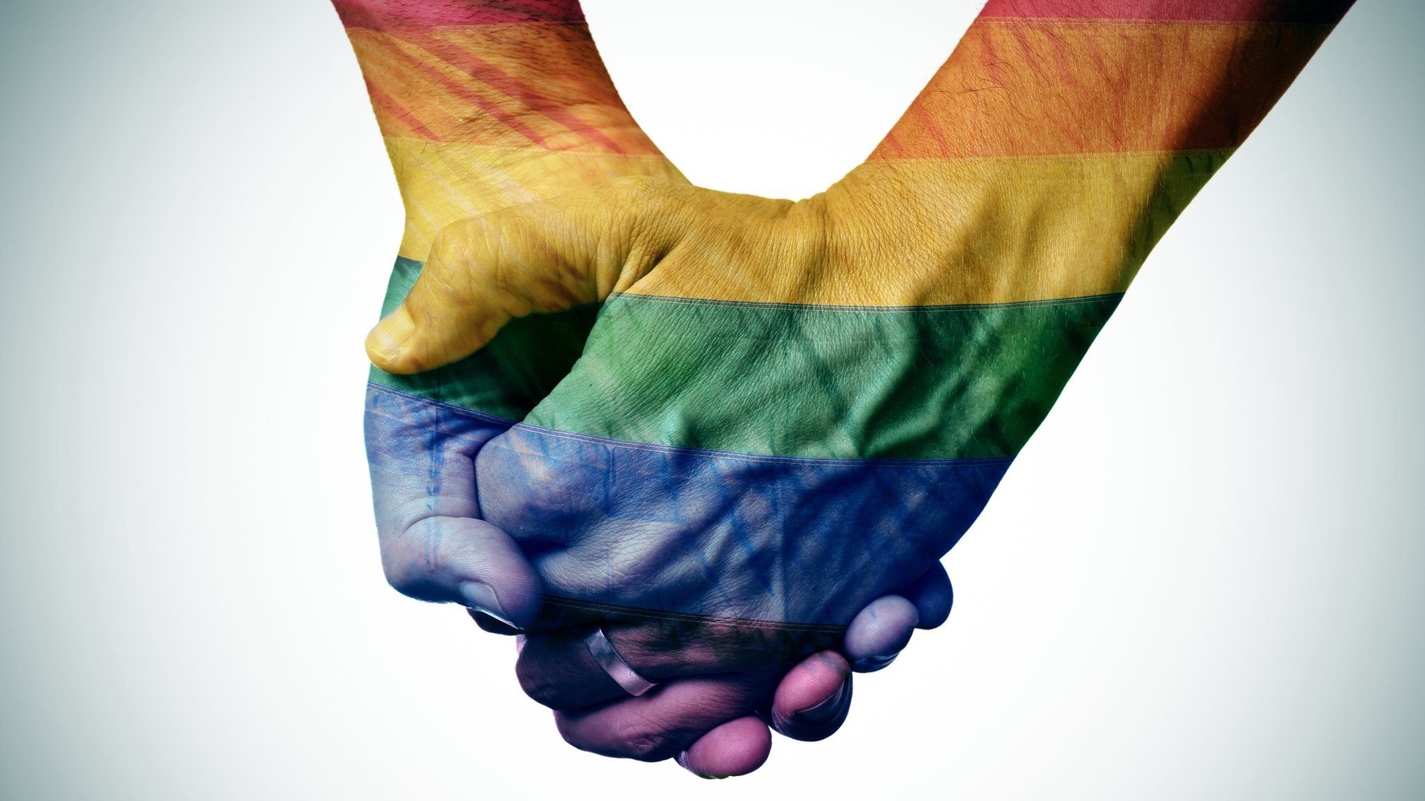 Two men holding hands with the rainbow flag projected onto them