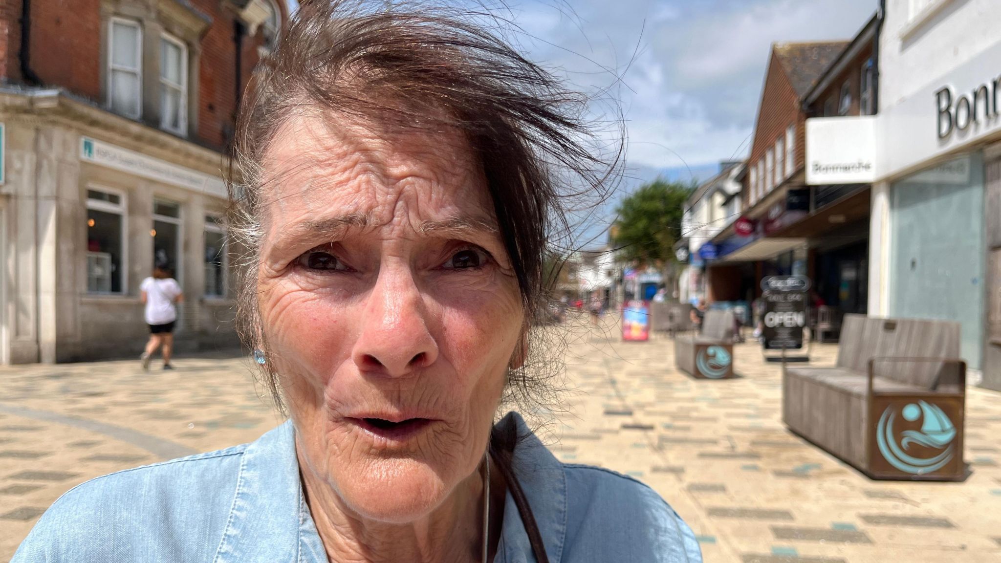 Susan Smith sits in the high street. Her dark hair is tied back and she wears a blue shirt.