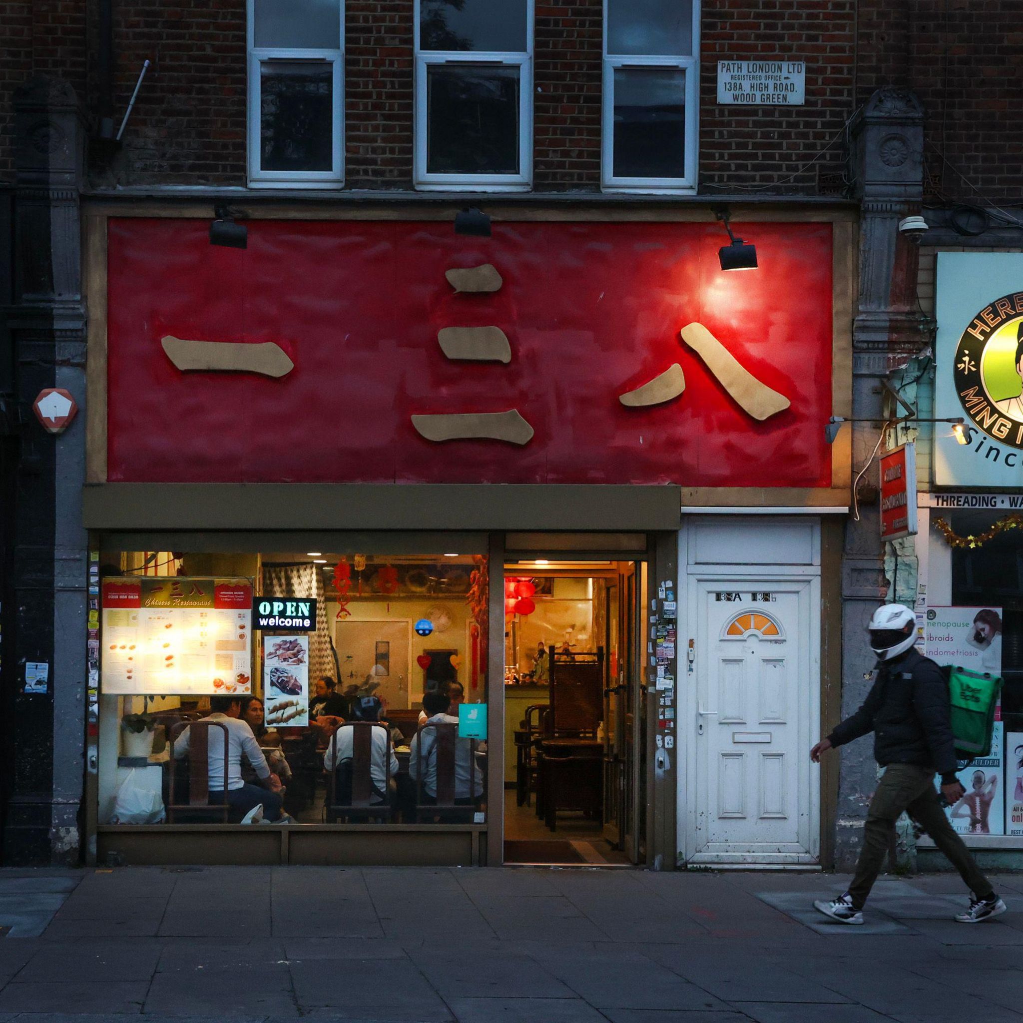 A Uber Eats delivery driver with a backpack walks past the front of a Chinese takeaway