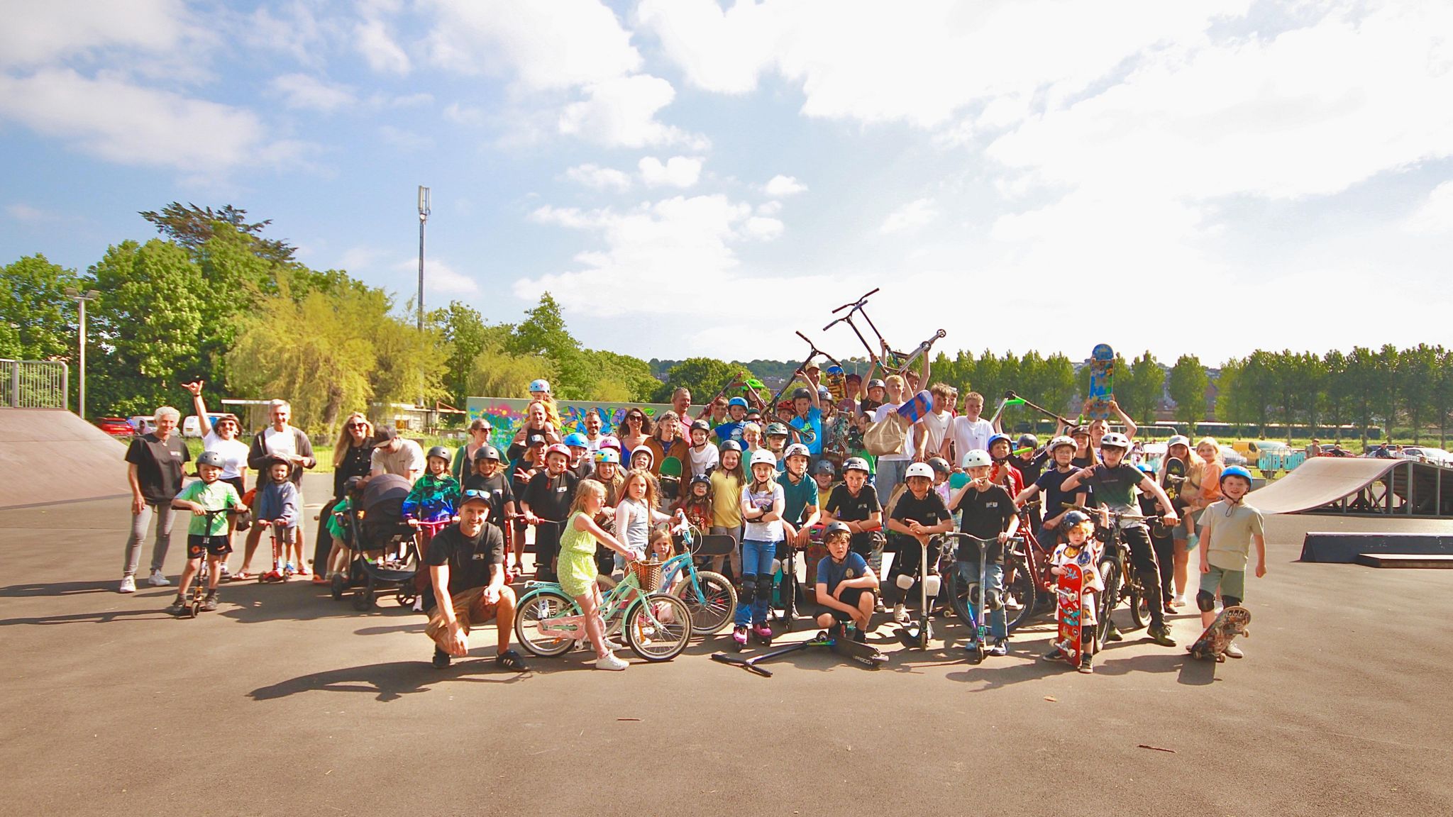 A community event with adults and children at the skatepark with their bikes and skateboards