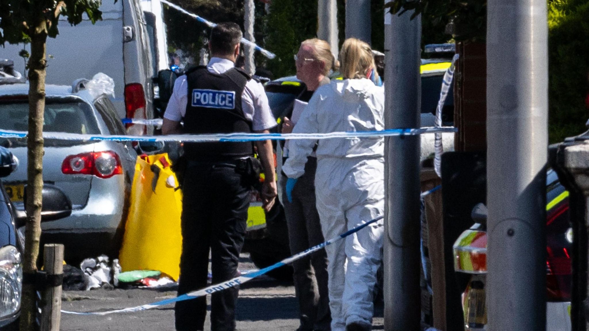 Police officers stand in a huddle talking behind a barrier of tape at the scene of the stabbing.