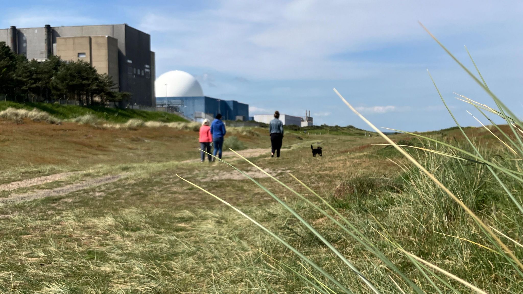 Three people walking on beach path in front of Sizewell A and B power stations