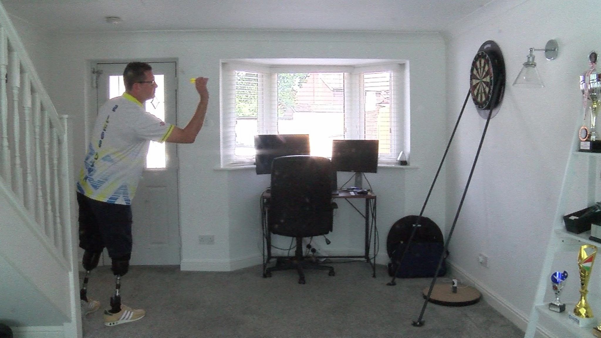 Steve North playing darts in the front room of a house.