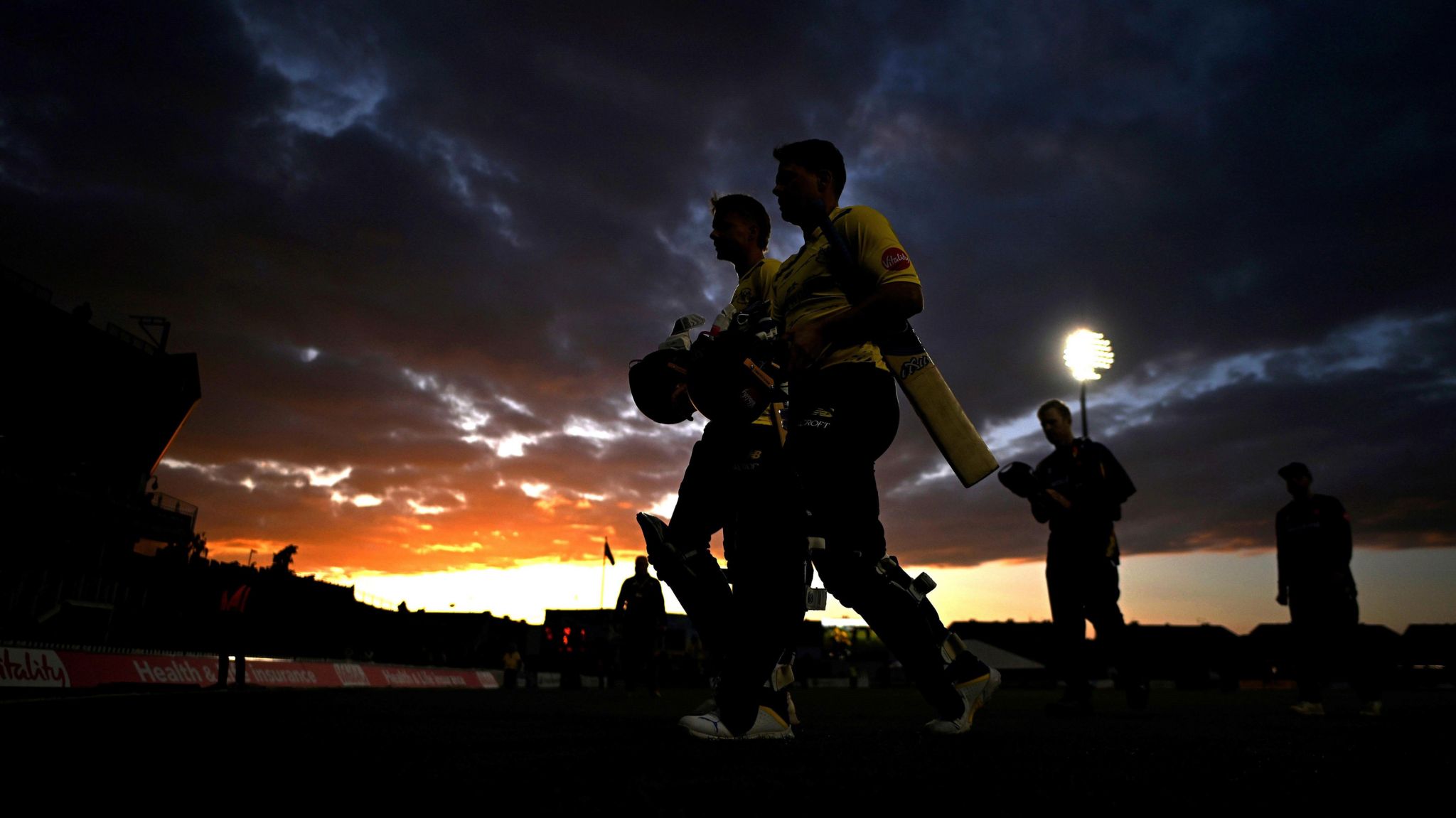 Essex and Gloucestershire players leave the pitch in Bristol in the sunset with the floodlights bright