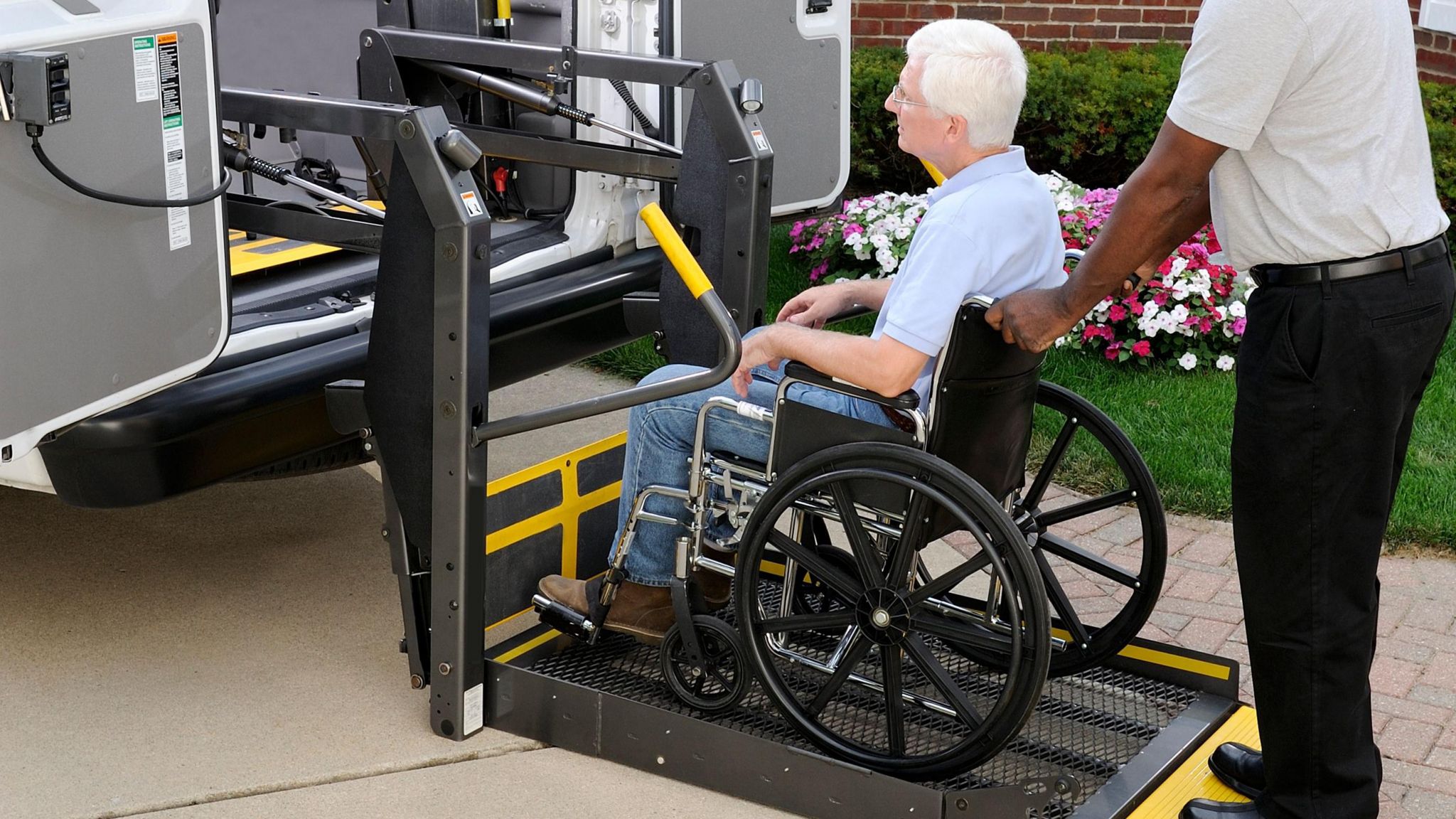 A man in a wheelchair being wheeled onto the back of a van by another man