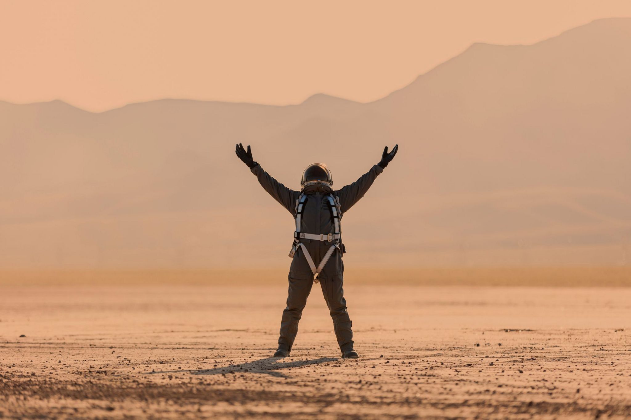  astronaut in space suit and helmet standing on Mars looking up with arms outstretched triumphantly with dust storm behind them, red orange all around.