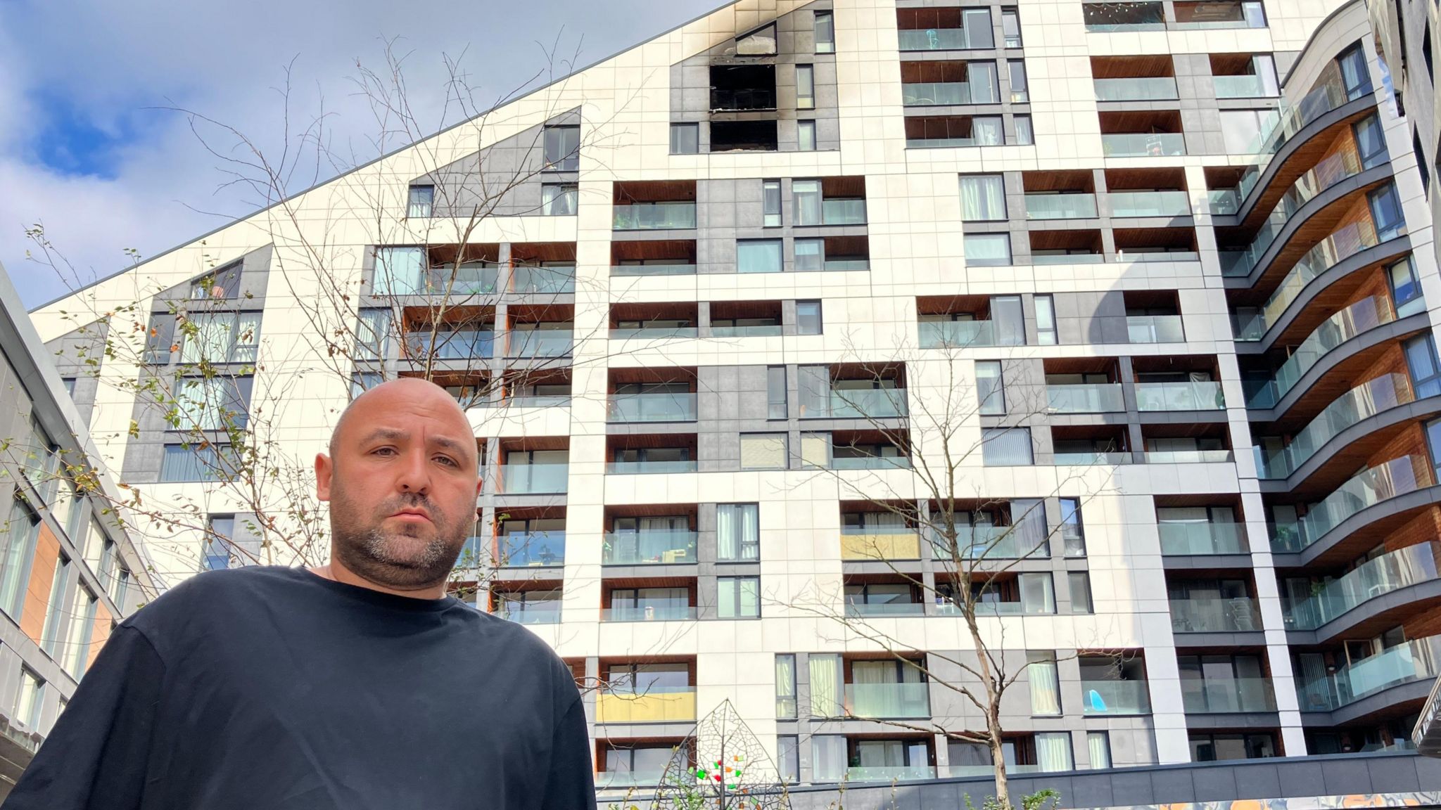 Josh Cope stands in front of Varney Court, a block of flats, with two balconies seen burned