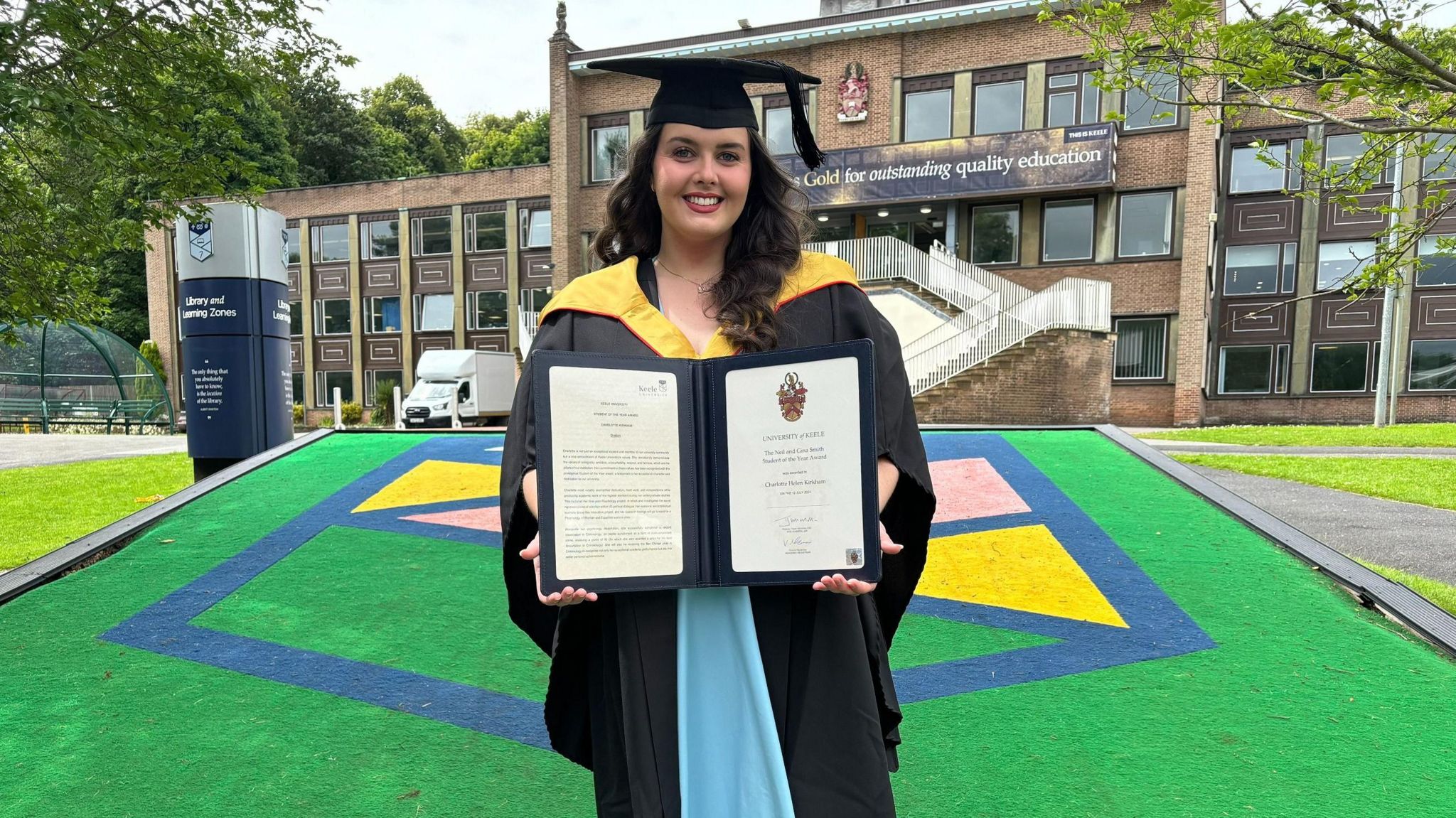 Charlotte Kirkham in a graduation robe with her award at Keele University