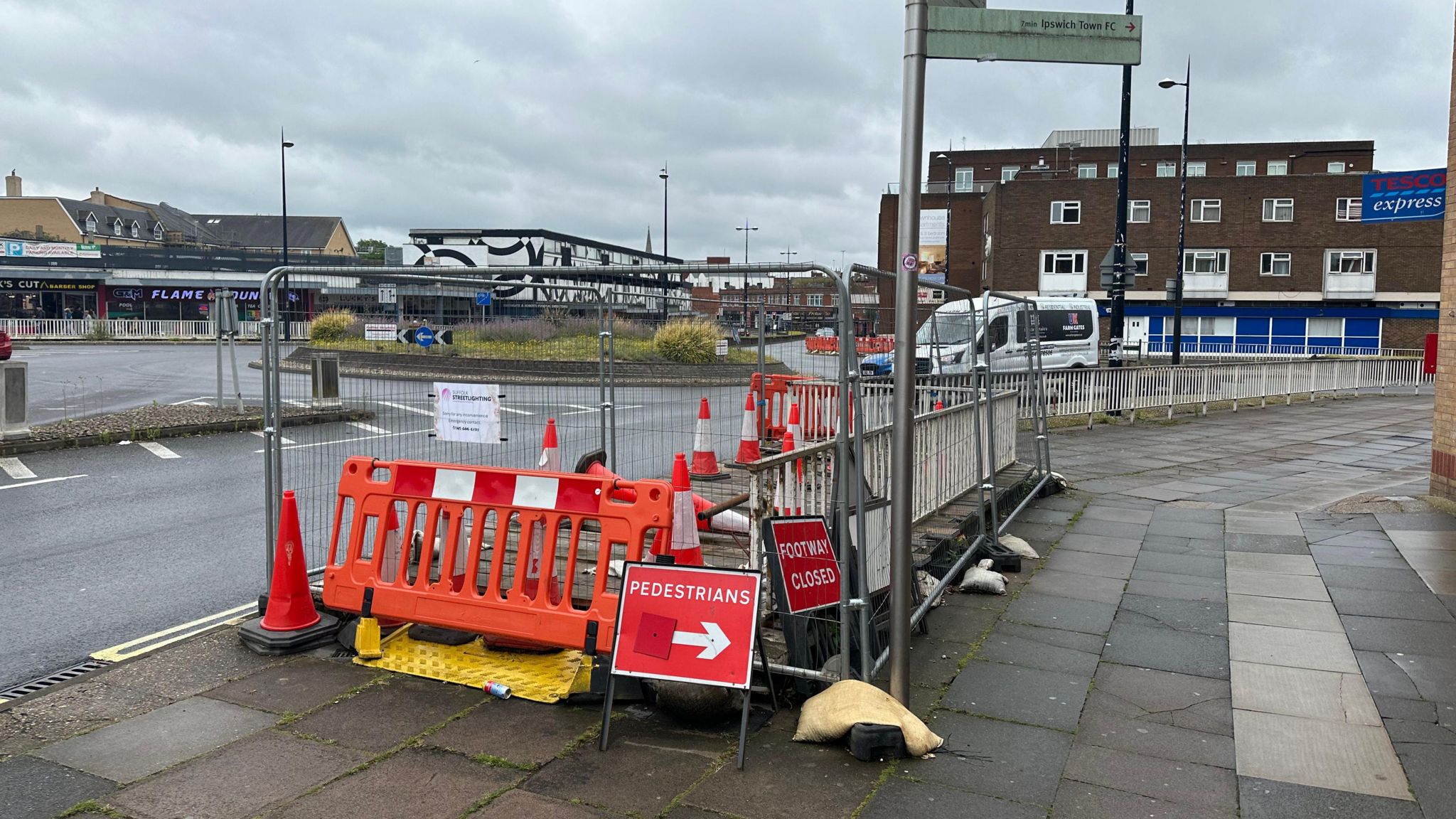 An entrance to the underpass blocked by silver and orange barriers, behind a sign reading "pedestrians" and with an arrow pointing to the right