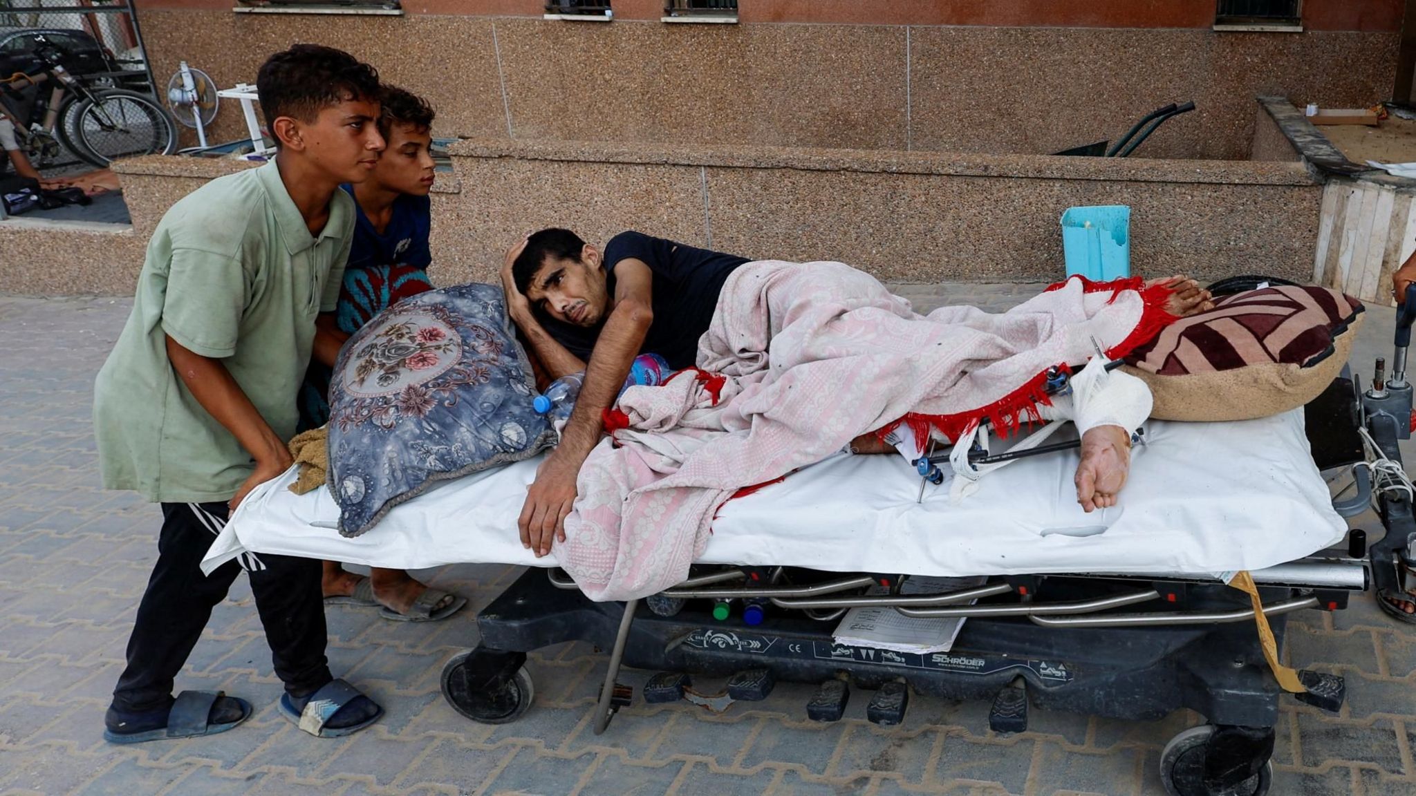 An injured Palestinian man is pushed on a hospital bed into Nasser hospital in Khan Younis, in the southern Gaza Strip, after being evacuated from the European Gaza hospital (2 July 2024)