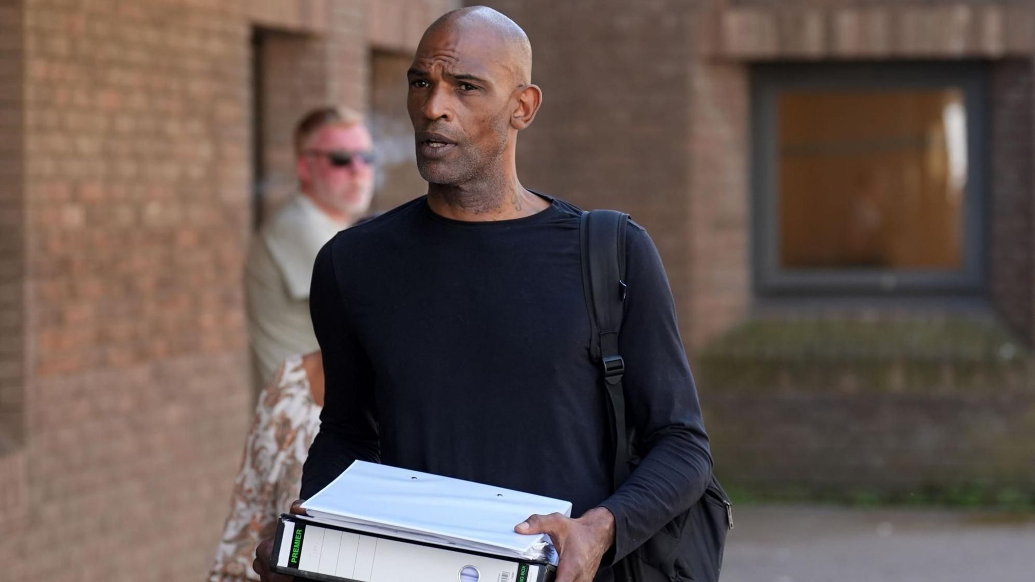 Matthew Martin wearing a black long-sleeved T-shirt and black rucksack, and holding two binders 