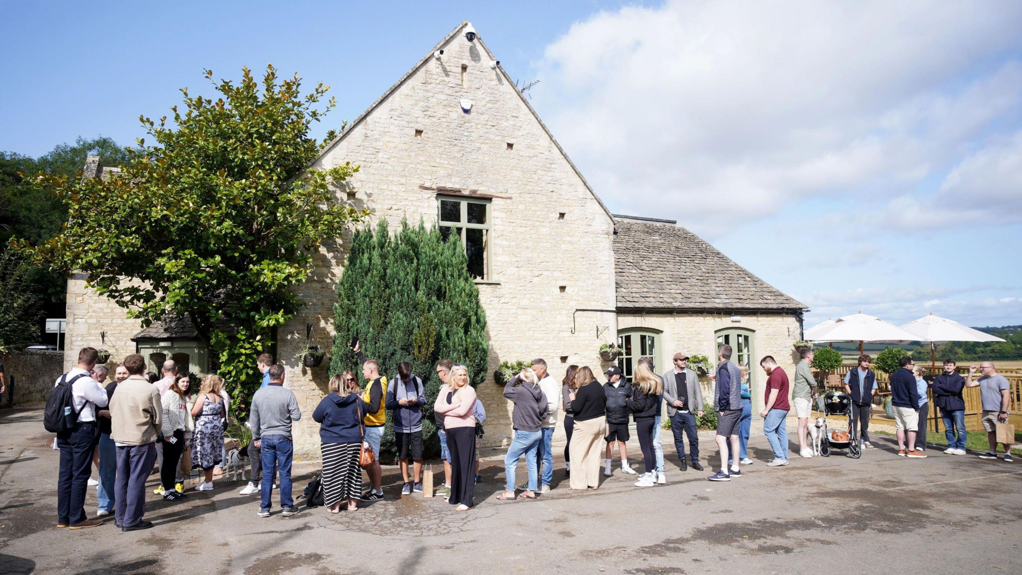 A queue made up of dozens of people outside of a cream-coloured pub.