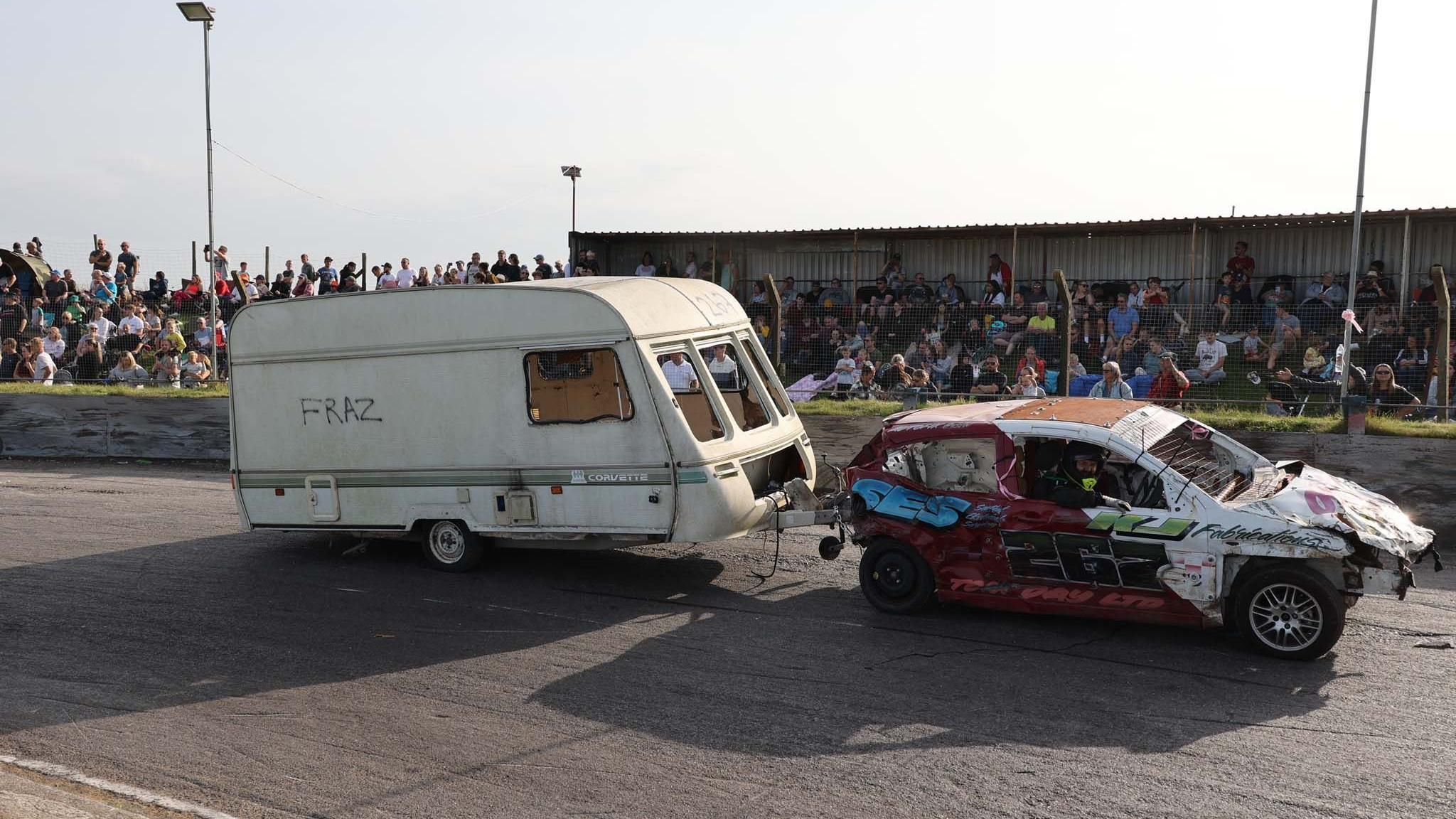 Caravan attached to race car with people watching behind barriers 