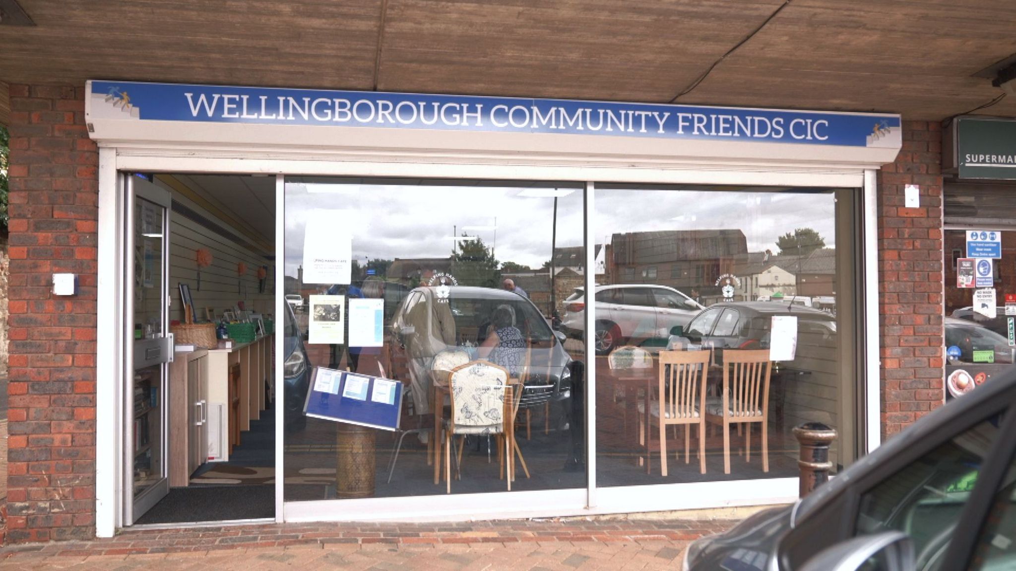 The frontage of the café - a red brick building with a blue sign with large glass windows 