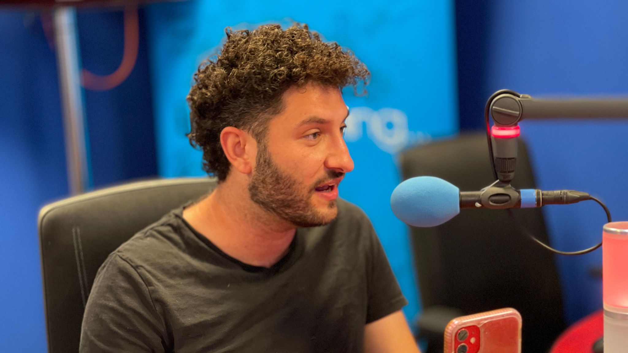 Billy Lockett with curly black hair and a black tee shirt, talking into a radio studio microphone