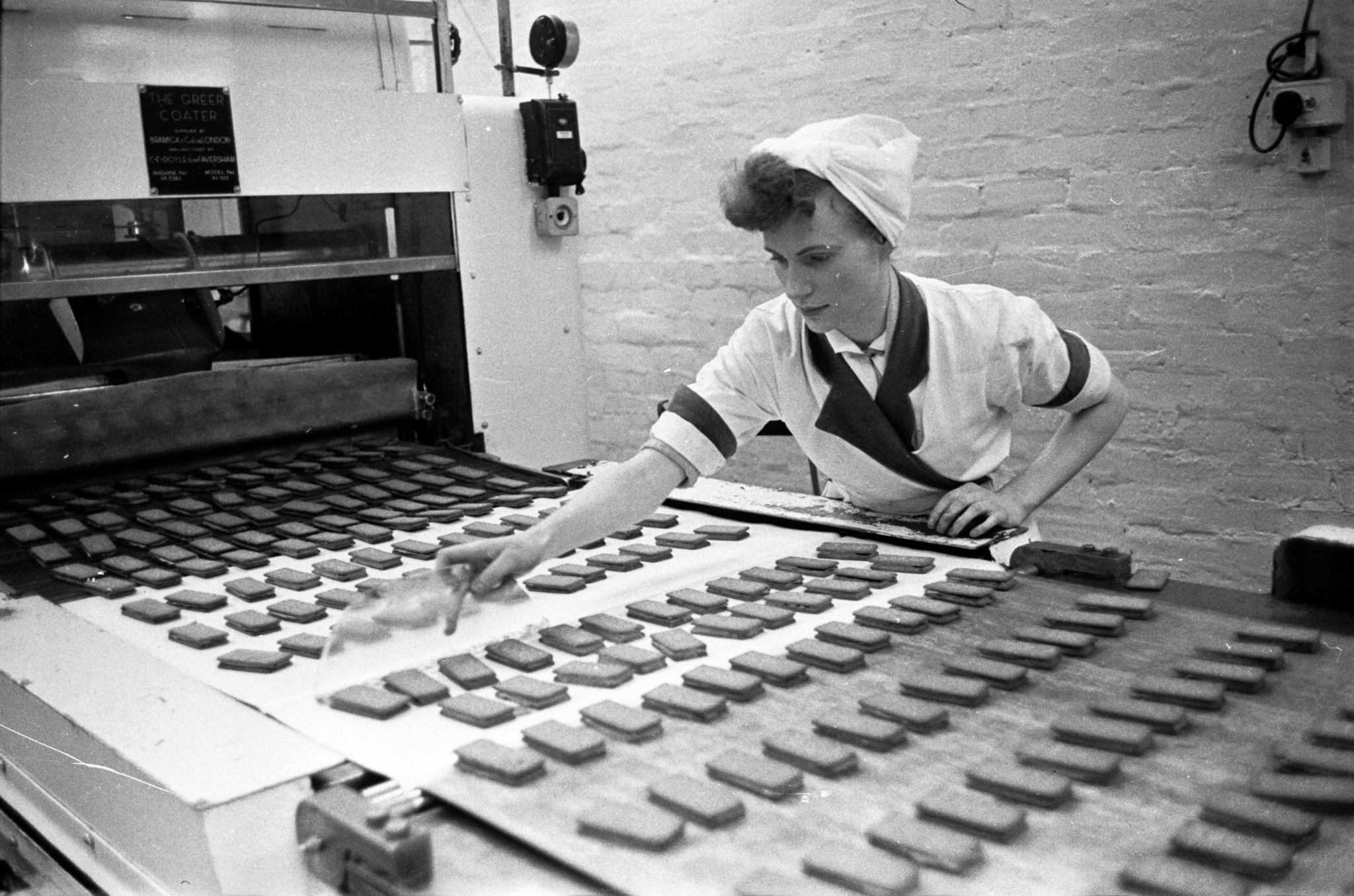 20th August 1955: A worker checking the quality of biscuits on a conveyor belt in the Glengarry Bakery of William Macdonald and Sons, Glasgow. This company's 24-hour production line generates a constant stream of biscuits and produces a quarter of Britain's total chocolate biscuit output. Original Publication: Picture Post - 7942 - Let Glasgow Flourish! - pub. 1955 (Photo by Haywood Magee/Picture Post/Hulton Archive/Getty Images)