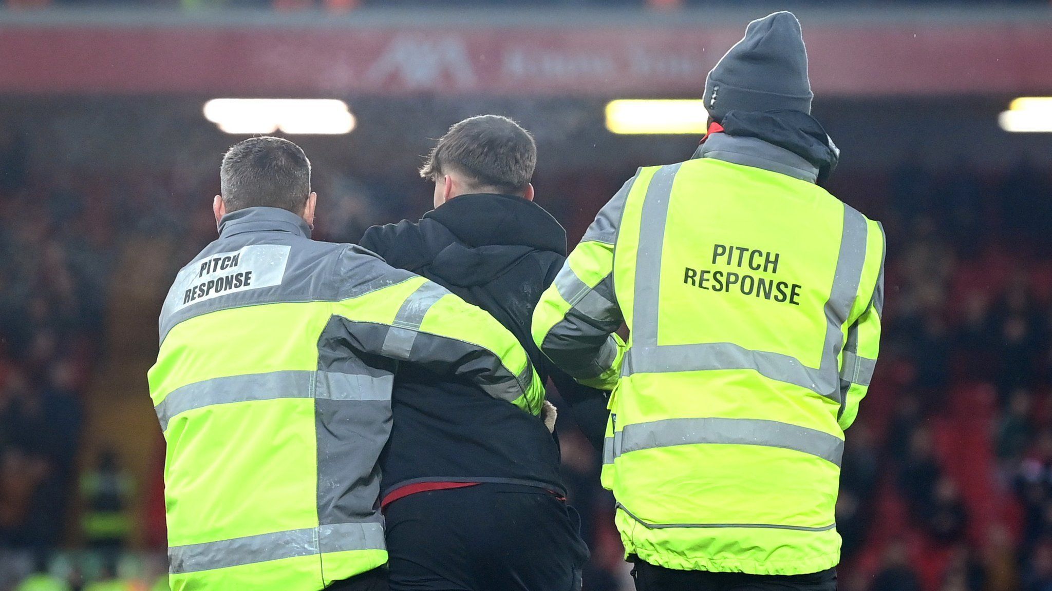 Two stewards tackling a pitch invader during a Premier League game