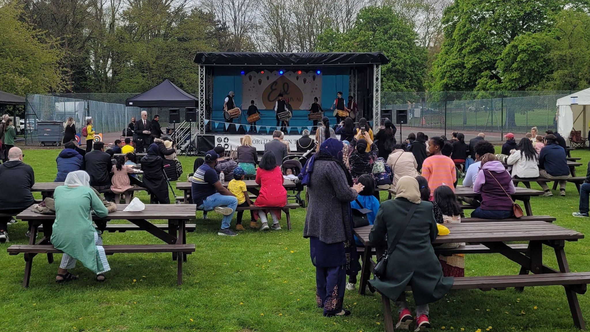 People on picnic benches watching performers on stage at Northampton Eid Festival 2023