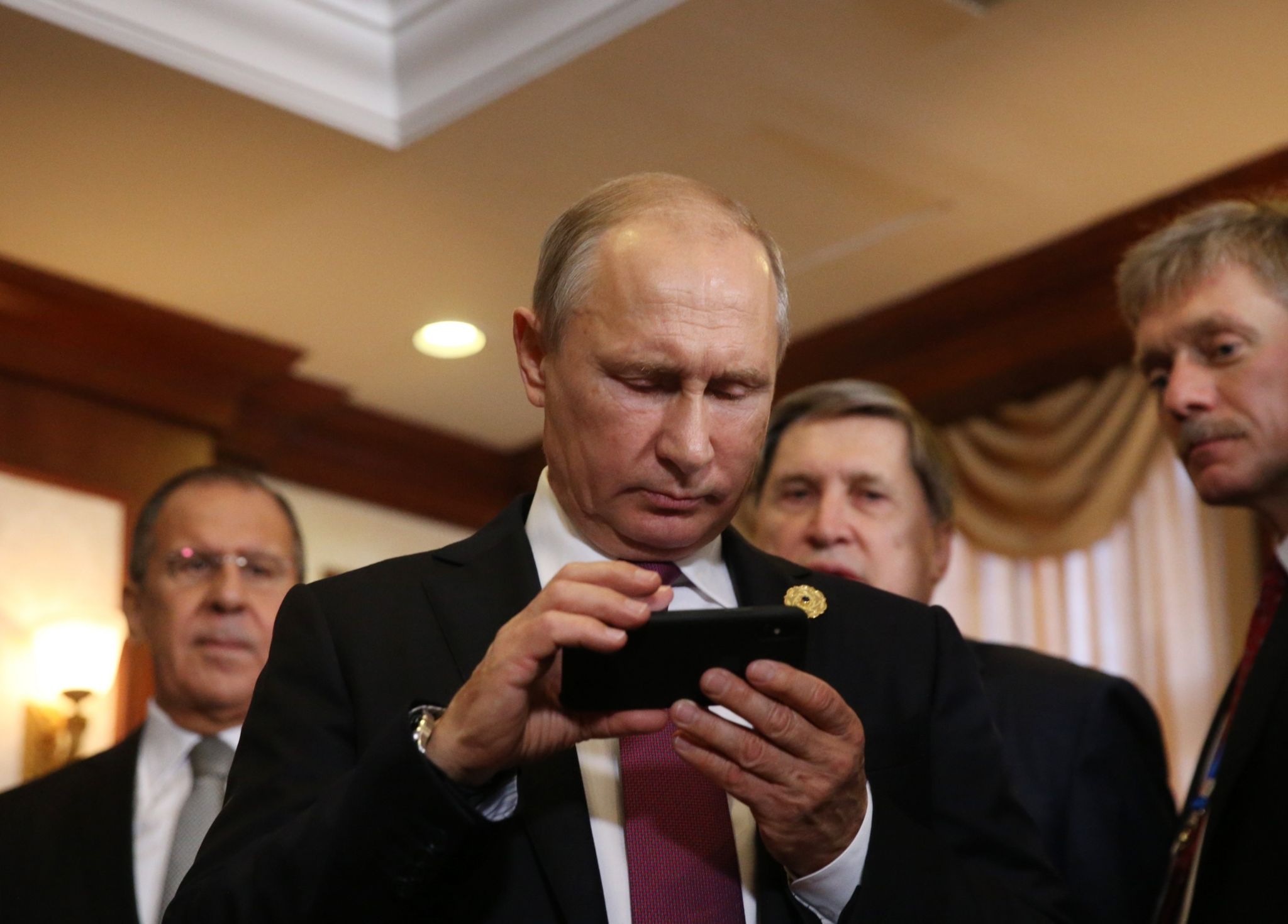 Владимир Путин осматривает iPhone в компании пресс-секретаря Дмитрия Пескова (справа) и министра иностранных дел Сергея Лаврова (слева)