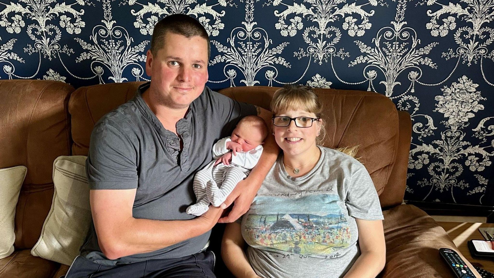 A man, baby and a woman sit on a sofa