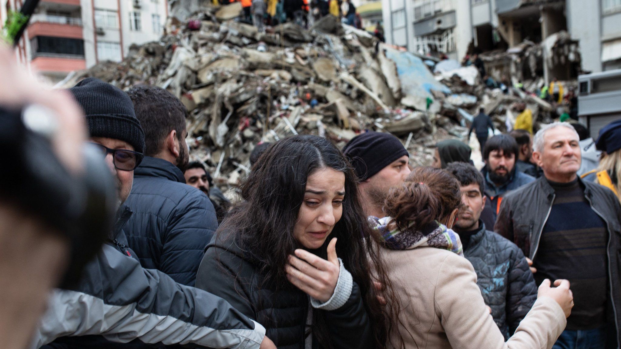 A woman reacts as rescuers search for survivors through the rubble of collapsed buildings in Adana