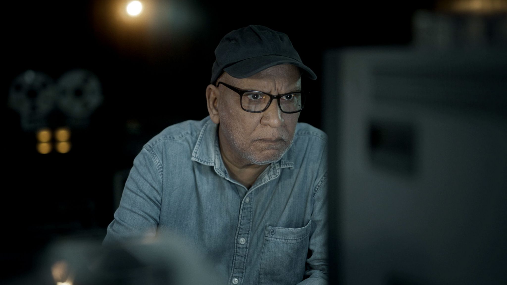 Veteran journalist Amitabh Parashar leans in to watch a monitor playing back the interviews he did with Indian midwives in the 1990s. The room is dark - his face illuminated by the screen.